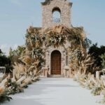 Beautiful outdoor wedding aisle with floral decorations leading to a stone building under a clear sky.