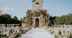 Beautiful outdoor wedding aisle with floral decorations leading to a stone building under a clear sky.