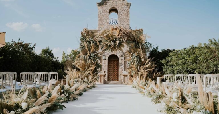 Beautiful outdoor wedding aisle with floral decorations leading to a stone building under a clear sky.