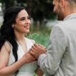 A lovely couple in elegant attire sharing a joyful moment outdoors in a lush garden setting.
