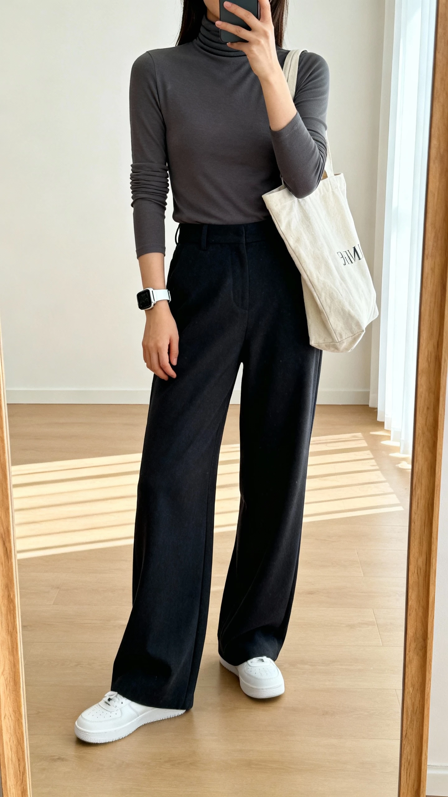 Casual iPhone mirror selfie of a woman in a fitted turtleneck with wide-leg trousers and clean white sneakers, sporty watch, canvas tote, face not visible, studio mirror, bright natural light, natural iPhone photo quality.