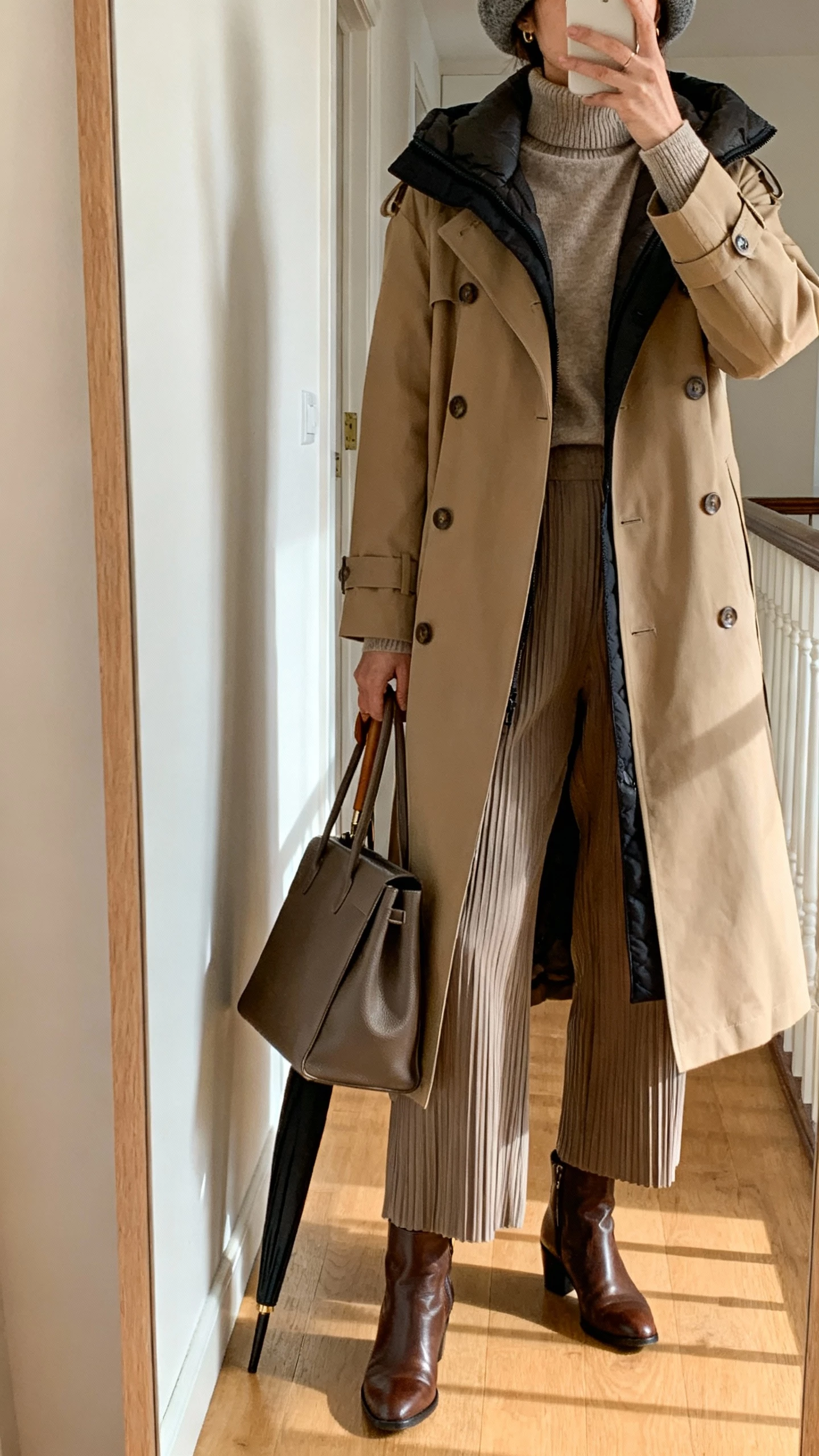 Hallway mirror selfie of a woman wearing a longline trench with removable lining over a merino turtleneck, pleated trousers, leather ankle boots, structured tote, slim umbrella, wool beret, face not visible, shoulders-down crop, indoor daylight, natural iPhone photo.