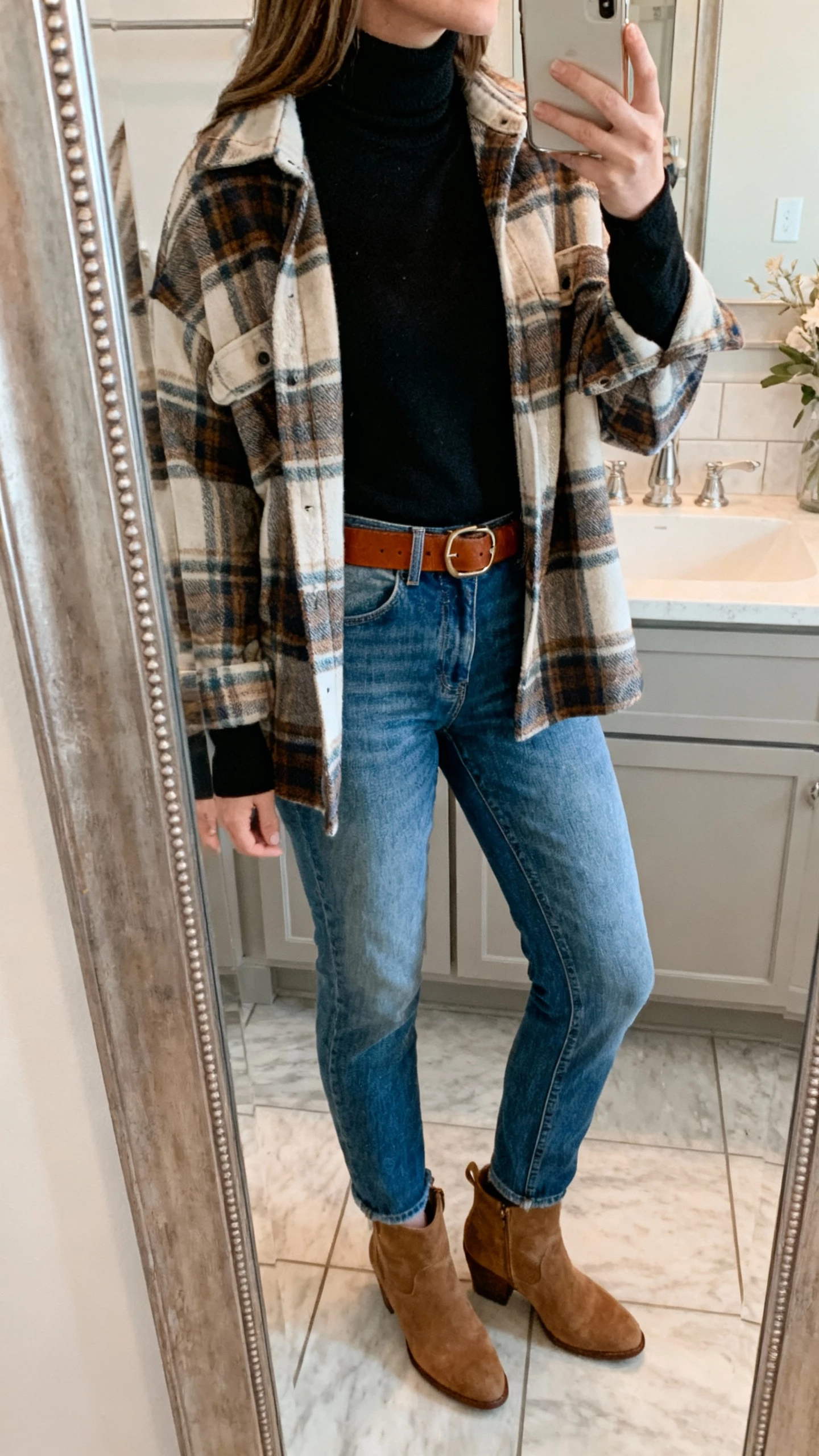 iPhone back-view mirror selfie of a woman layering a black turtleneck under a plaid flannel with classic blue jeans, brown belt, suede ankle boots, face not visible, bathroom mirror, soft natural light, casual iPhone photo