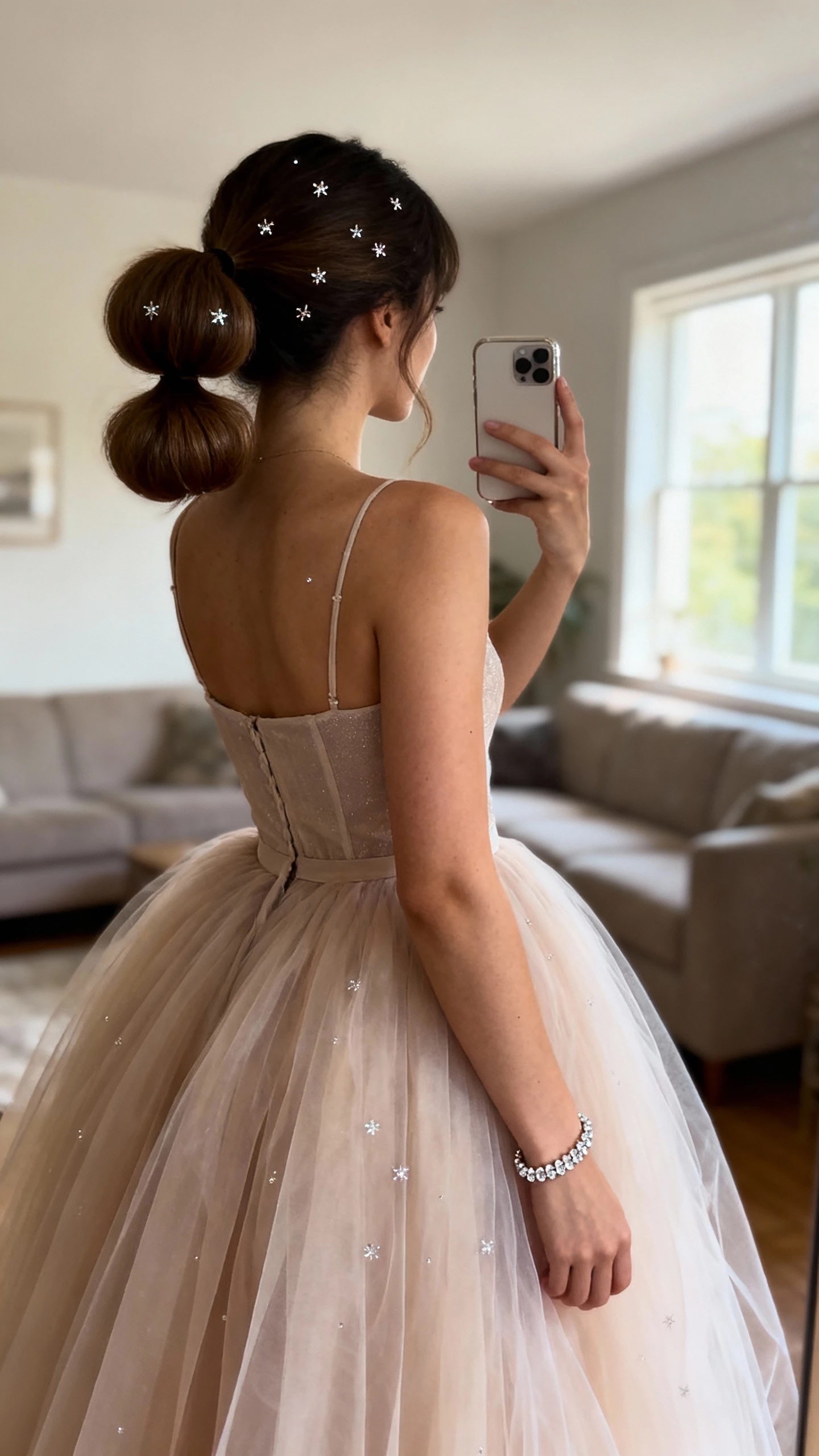 iPhone back-view selfie of a woman with a bubble ponytail and subtle sparkle pins, tulle ballgown skirt with fitted bodice, fine crystal bracelet, face not visible, taken in a softly lit living room near a window, natural daylight, casual iPhone look