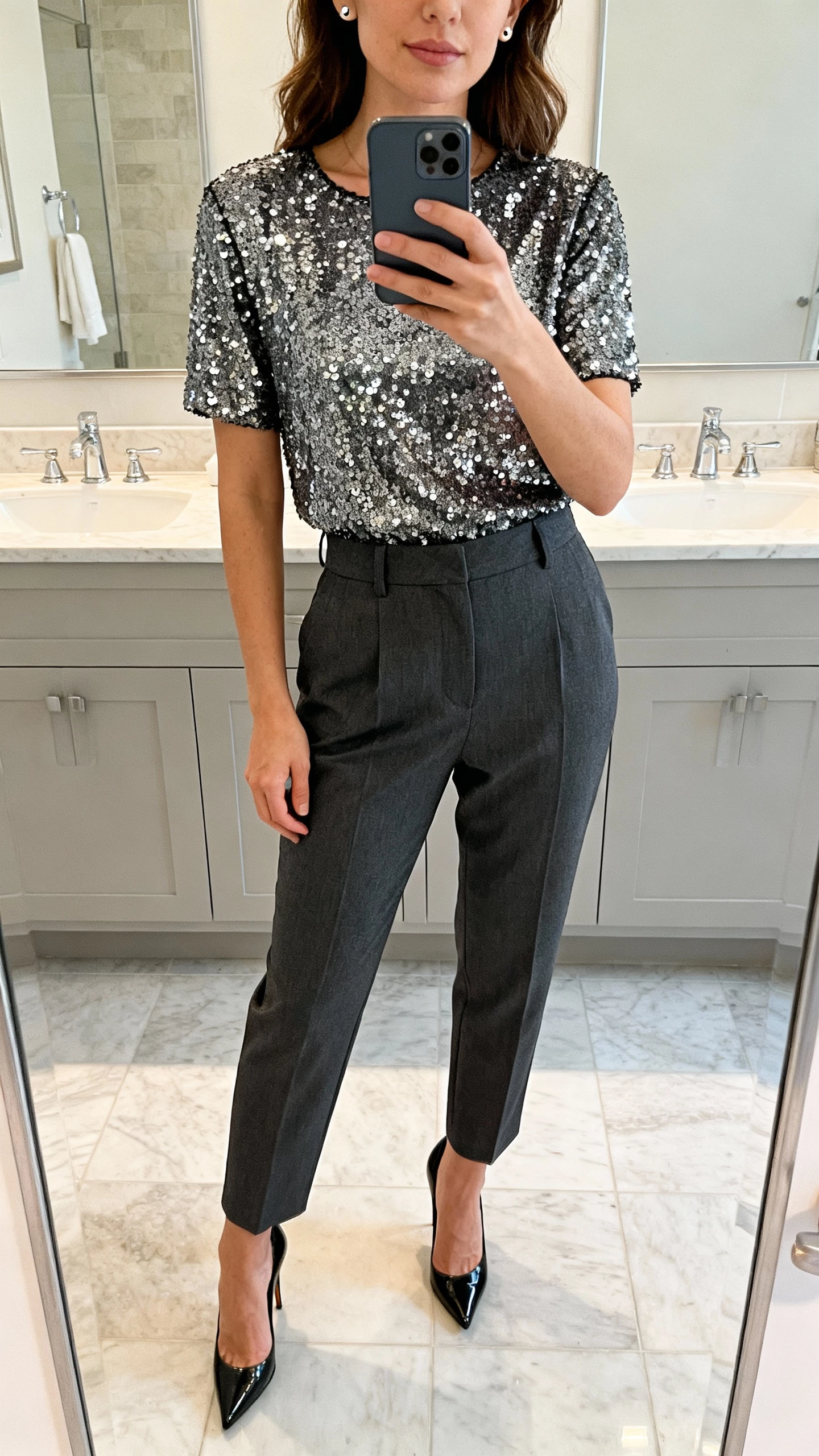 iPhone bathroom mirror selfie of a woman in a sequined top, high-waisted tailored trousers, sleek stilettos, minimal stud earrings, face not visible, cropped at chin, soft overhead lighting, natural iPhone quality.
