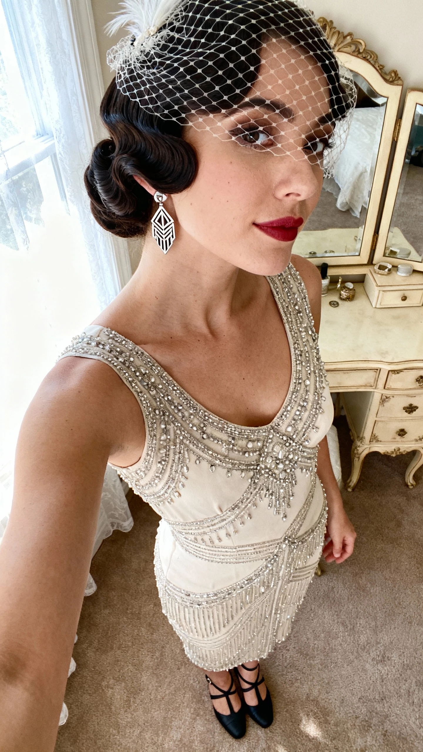 iPhone cropped-at-neck selfie of a woman with 1920s finger waves and a birdcage veil, beaded sheath dress, art deco earrings, T-strap heels; face not visible, vintage-style vanity, soft window light, natural iPhone photo quality.