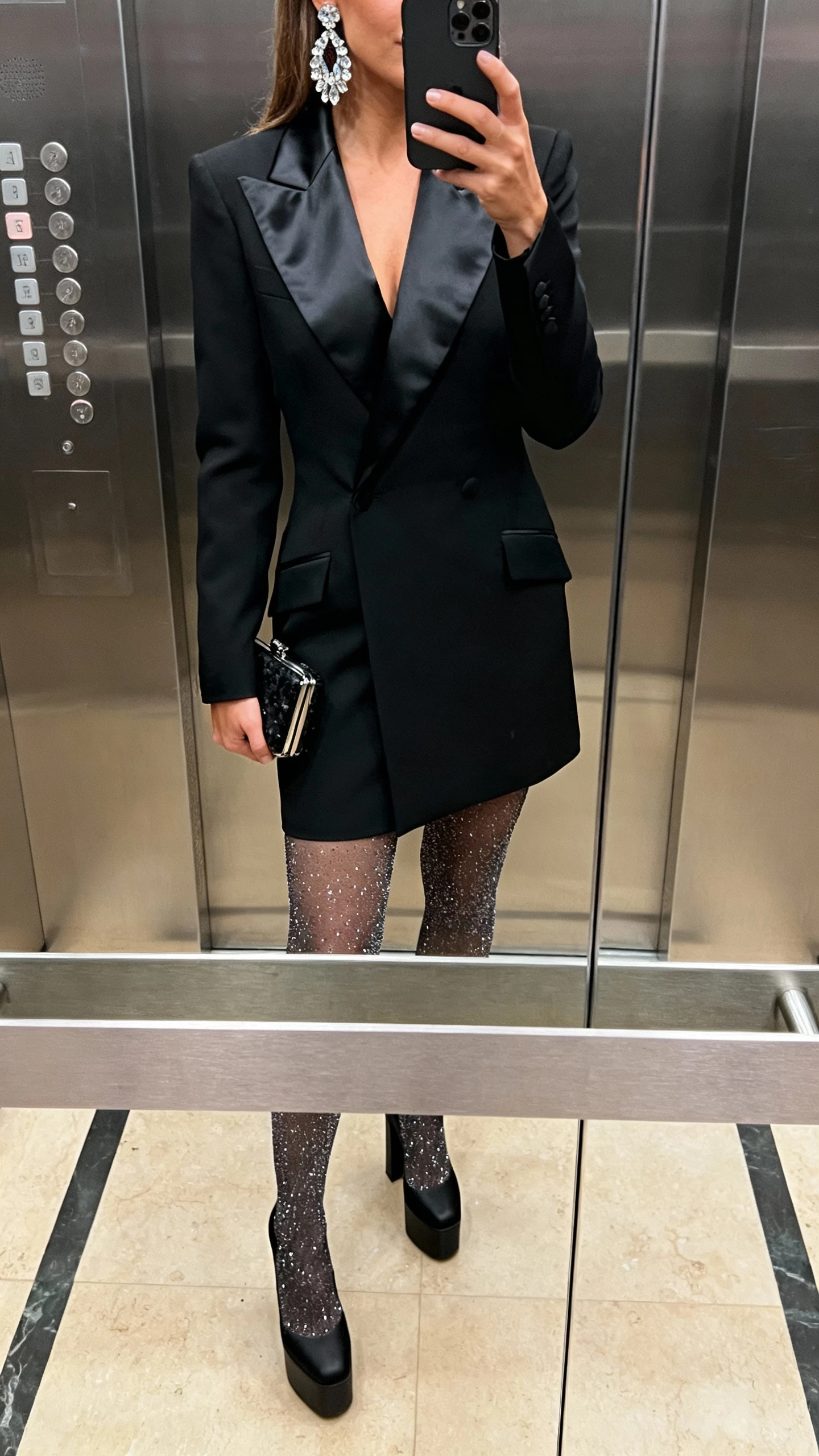 iPhone elevator mirror selfie of a woman wearing a black tuxedo dress with satin lapels and sparkle tights, platform heels, statement crystal earrings, mini clutch, face not visible, indoor lighting, natural iPhone photo quality.