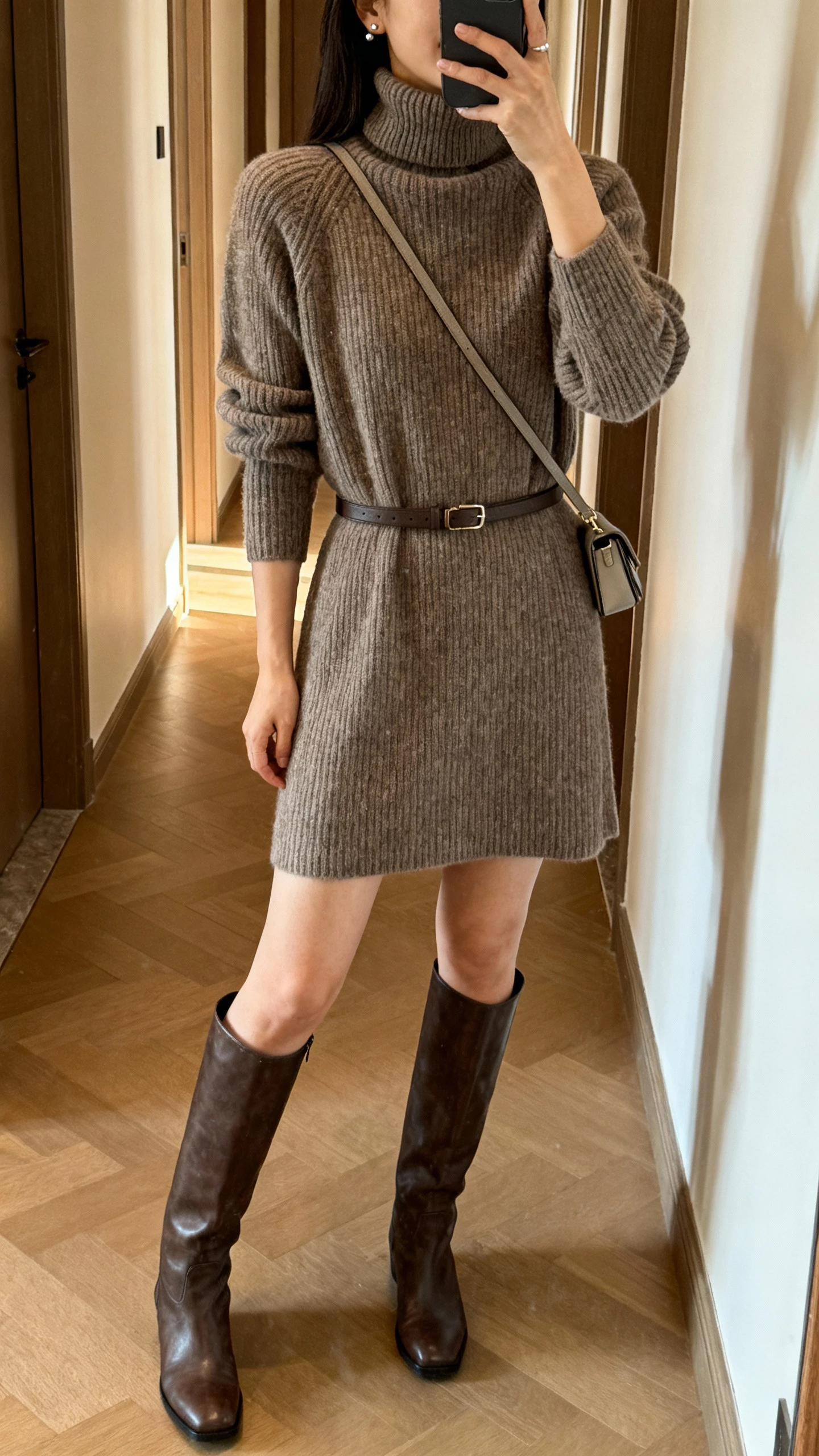 iPhone hallway mirror selfie of a woman in a turtleneck knit dress with knee-high boots and a slim belt, small crossbody bag and minimal studs, face not visible, warm indoor lighting, casual iPhone aesthetic