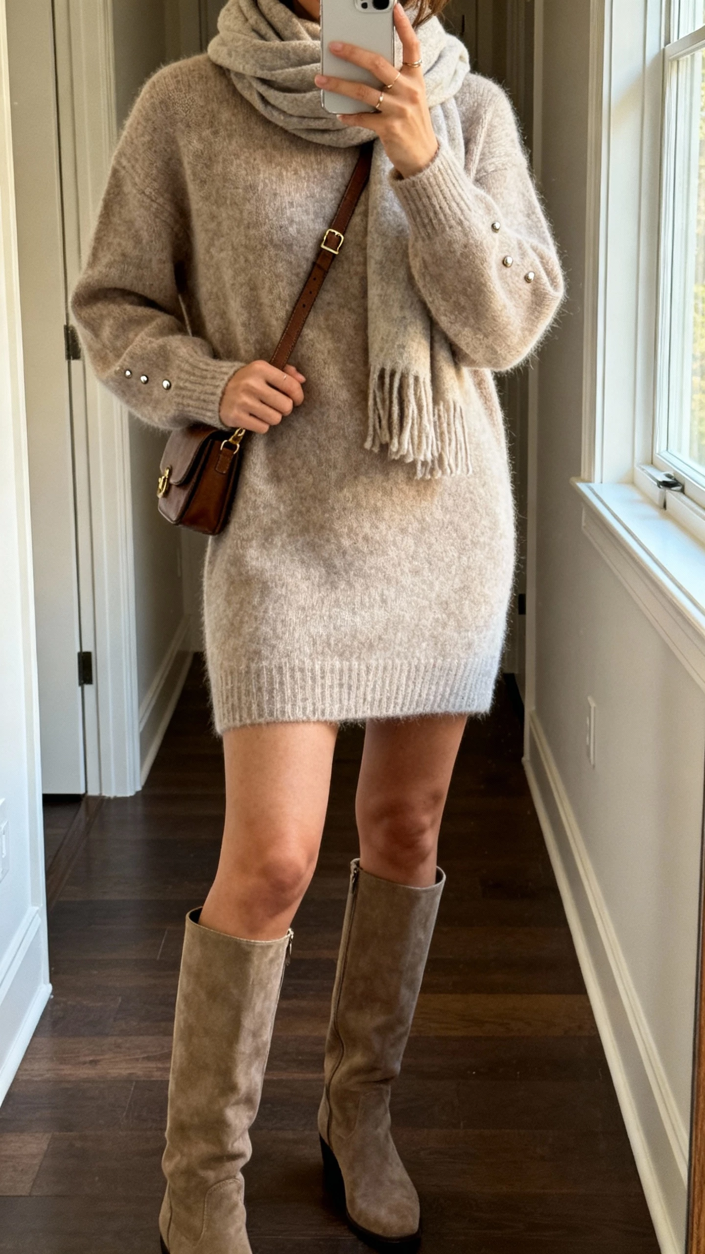 iPhone hallway mirror selfie of a woman wearing a luxe sweater dress, knee-high boots, cozy scarf, simple studs, crossbody bag, face not visible, soft afternoon window light, casual iPhone photo