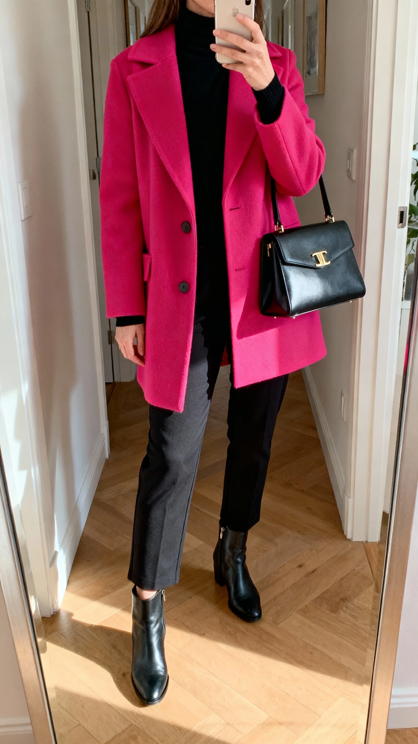 iPhone hallway mirror selfie of a woman wearing an all-black base (black turtleneck and black trousers) with a pop-of-color coat, ankle boots, structured handbag, face not visible, natural afternoon light, natural iPhone photo quality.