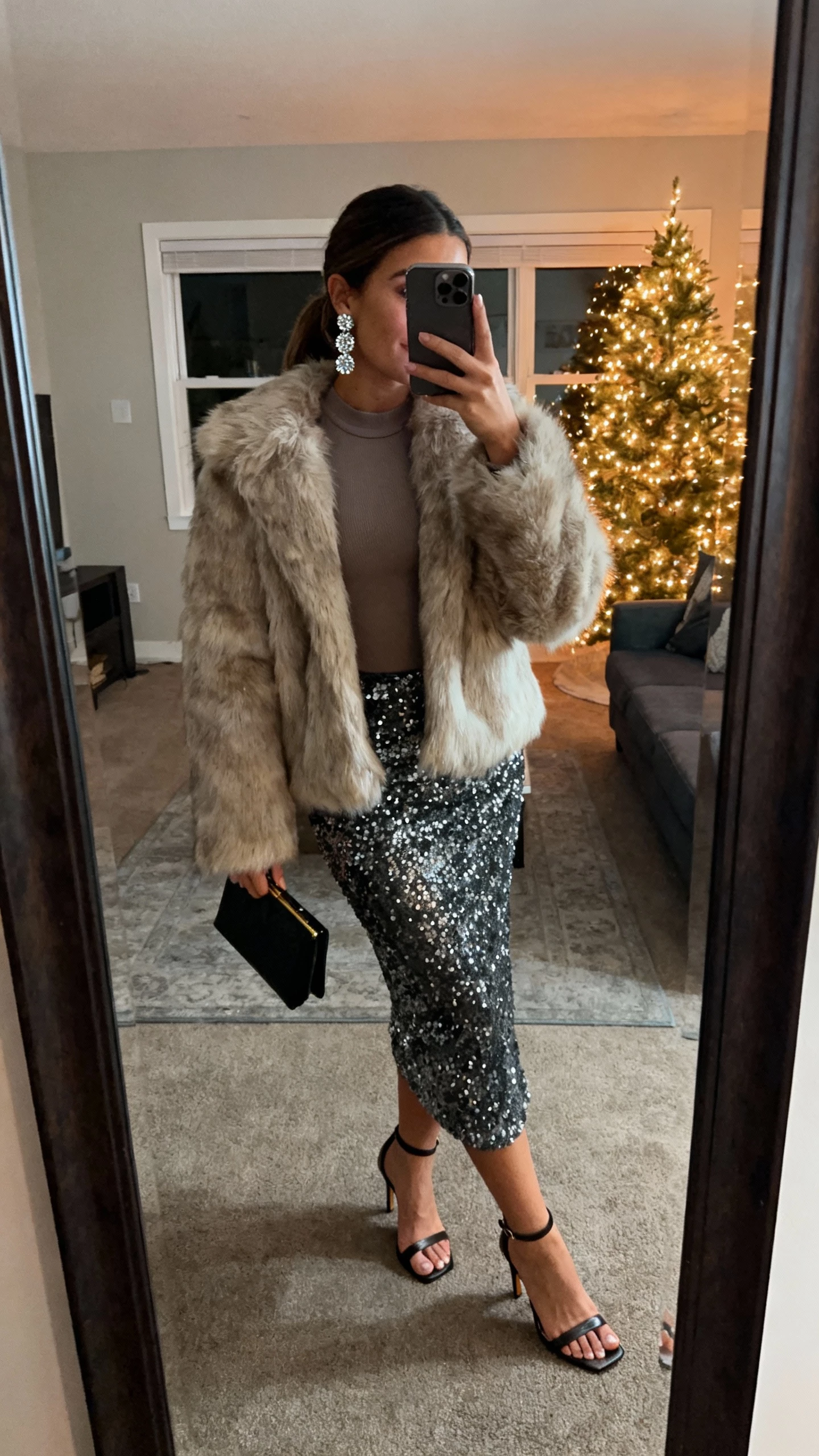 iPhone living-room mirror selfie of a woman in a plush fur jacket over a sequin skirt, fitted top, heeled sandals, clutch, sparkly earrings, face not visible, evening indoor lighting with tree lights, natural iPhone photo quality.