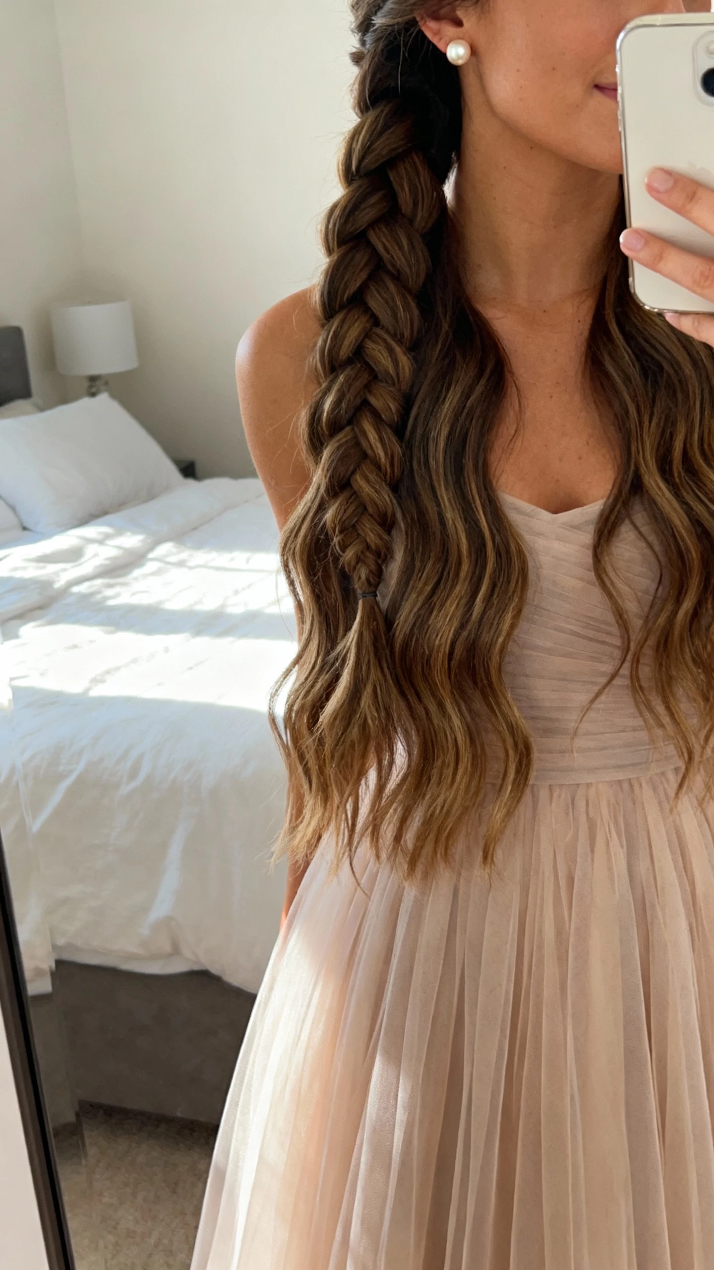 iPhone mirror selfie of a cascading waterfall braid flowing over loose waves, paired with a tulle A-line dress and pearl stud earrings, face not visible, bedroom mirror in soft morning light, natural iPhone photo quality.