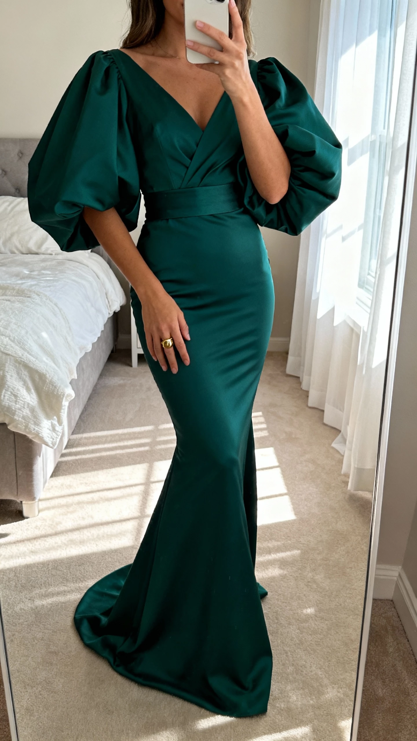 iPhone mirror selfie of a woman in a deep jewel-toned (emerald) mermaid dress with dramatic statement sleeves and fitted waist, gold ring, face not visible, bedroom mirror, morning window light, natural iPhone aesthetic.