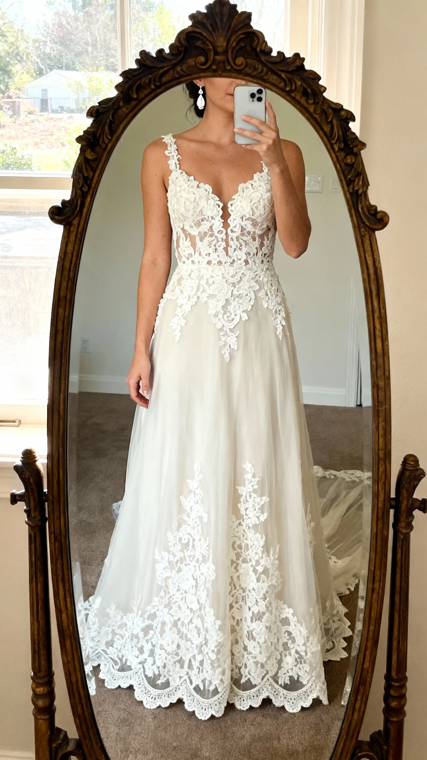 iPhone mirror selfie of a woman in old-world Alençon lace wedding dress with bold lace appliqués, illusion neckline, scalloped hem, vintage-style drop earrings, face not visible, cropped at neck, antique-frame mirror, soft morning light, natural iPhone photo quality