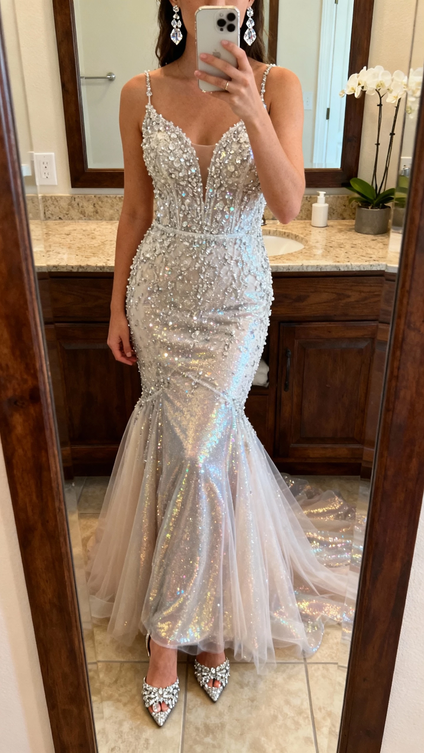 iPhone mirror selfie of a woman wearing a beaded mermaid wedding dress covered in sparkle with a fitted bodice and shimmer tulle skirt, crystal earrings and embellished heels, face not visible, bathroom mirror, warm indoor lighting, natural iPhone photo quality