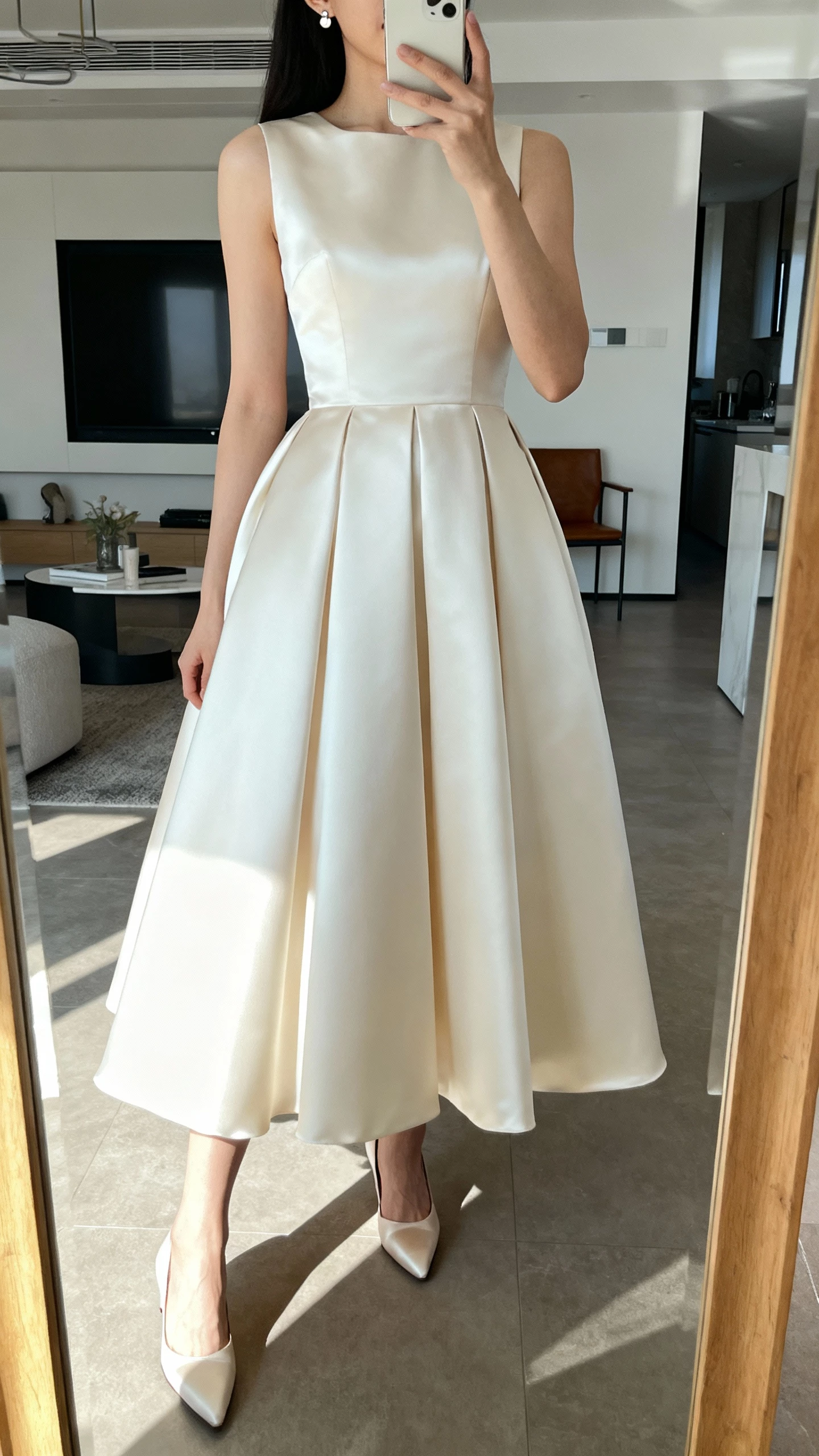iPhone mirror selfie of a woman wearing a minimalist clean silk ball gown with sleek A-line skirt, straight neckline, no embellishments, simple stud earrings, and satin heels, face not visible, cropped at neck, modern apartment mirror, natural daylight, iPhone photo quality
