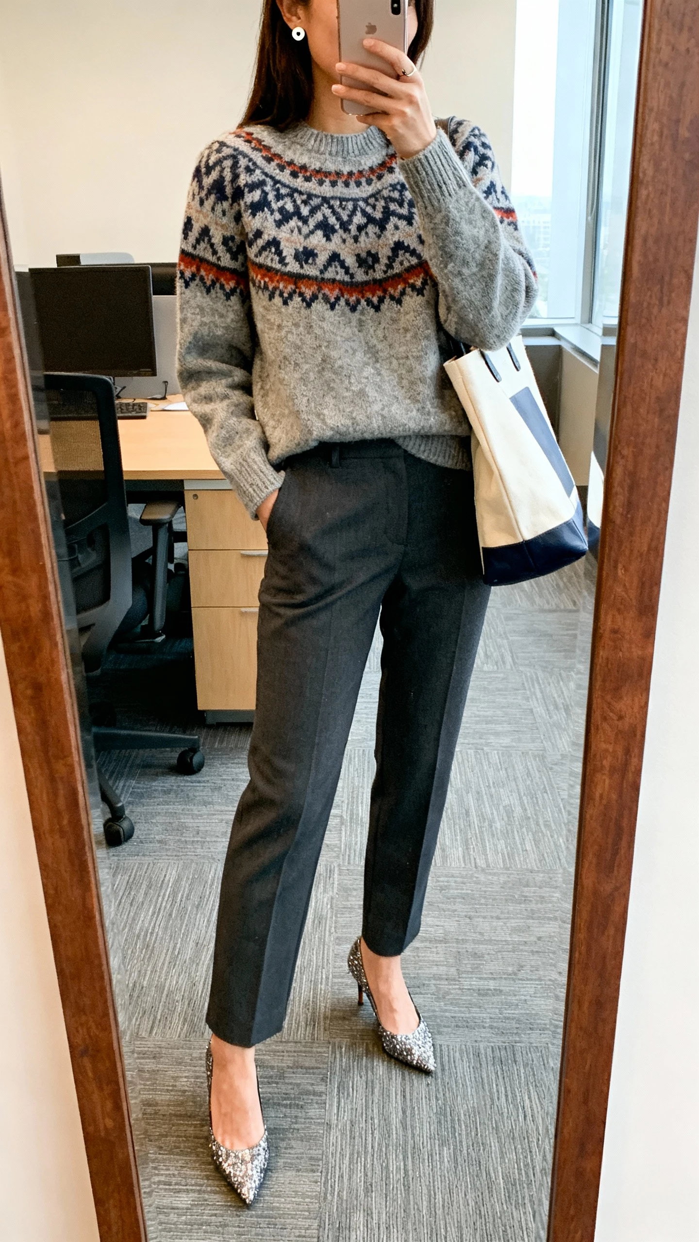 iPhone office mirror selfie of a woman in a statement sweater paired with tailored trousers and sparkly heels, simple stud earrings and a tote, face not visible, indoor lighting, natural iPhone photo quality.