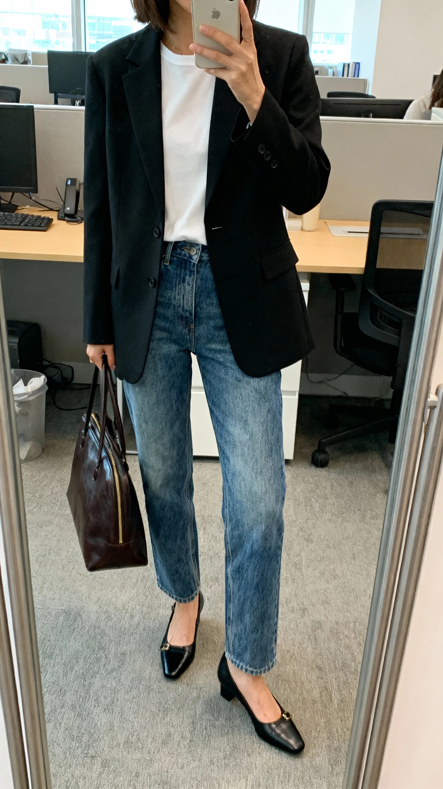 iPhone office mirror selfie of a woman in a tailored black blazer over vintage blue straight jeans, white tee, black slingback heels, leather tote, face not visible, morning office light, natural iPhone photo quality.