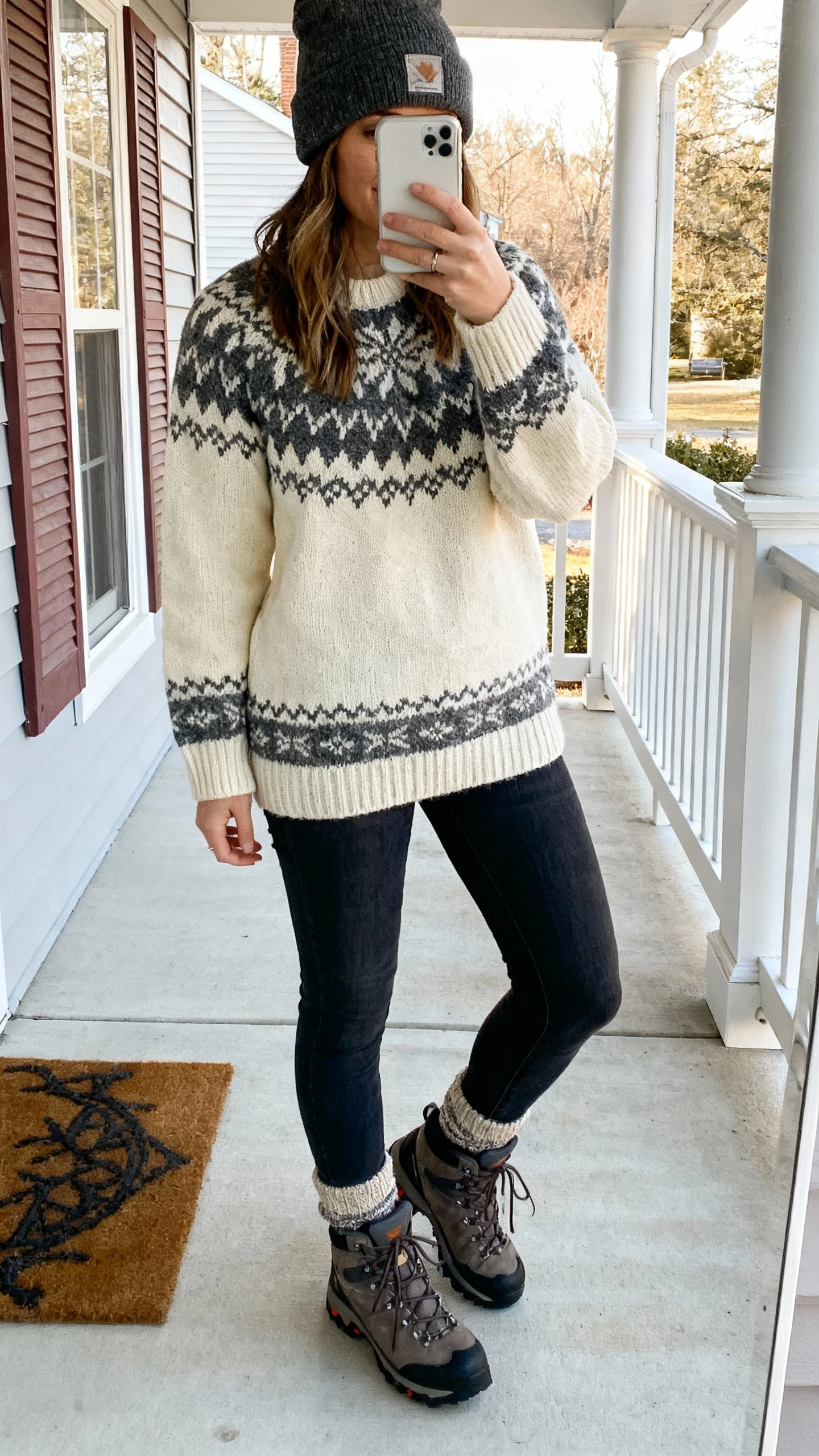 iPhone porch selfie of a woman wearing a cream-and-charcoal Fair Isle sweater, dark skinny jeans, hiking-inspired lace-up boots, beanie, wool socks peeking, face not visible, morning outdoor light, natural iPhone photo quality.