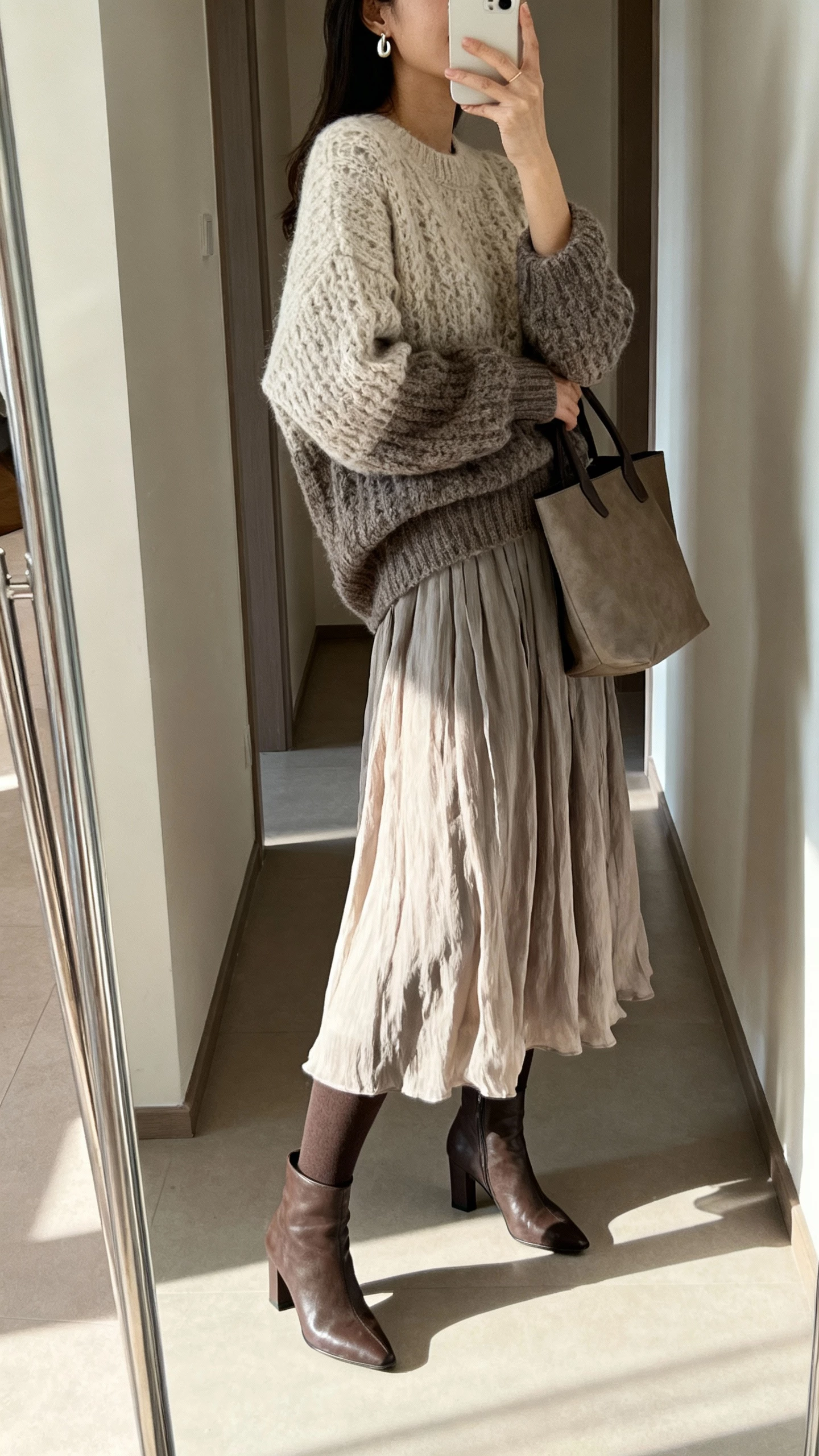 iPhone side-angle selfie of a woman wearing a flowy midi dress with a chunky knit sweater layered over it, tights and heeled boots, simple earrings and a tote, face not visible, hallway mirror, morning light, casual iPhone aesthetic.