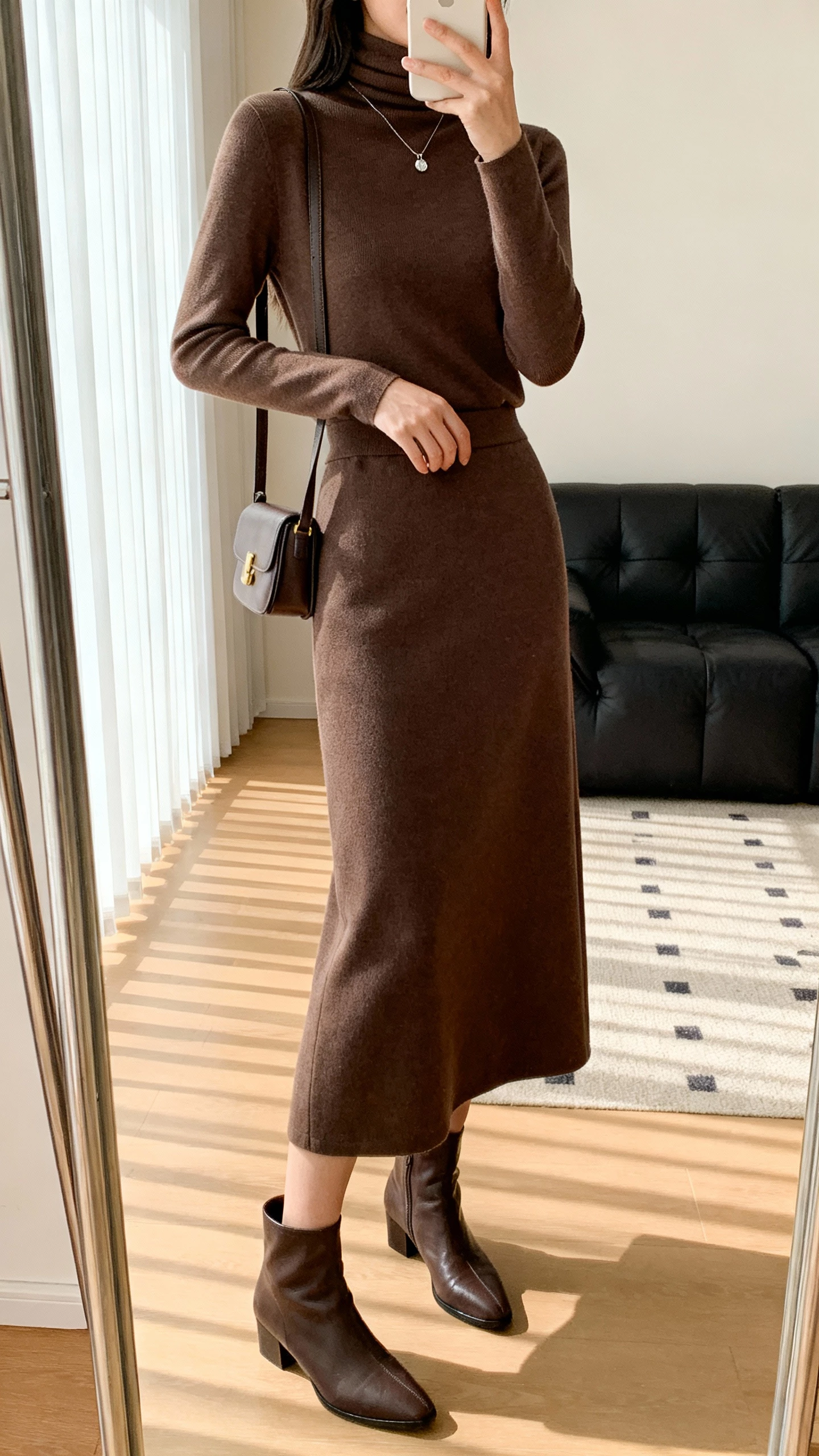 iPhone side-angle selfie showing a woman in a matching midi skirt set with a slim turtleneck, ankle boots, small shoulder bag, subtle pendant necklace, face not visible, living room mirror, natural daylight, natural iPhone photo quality.