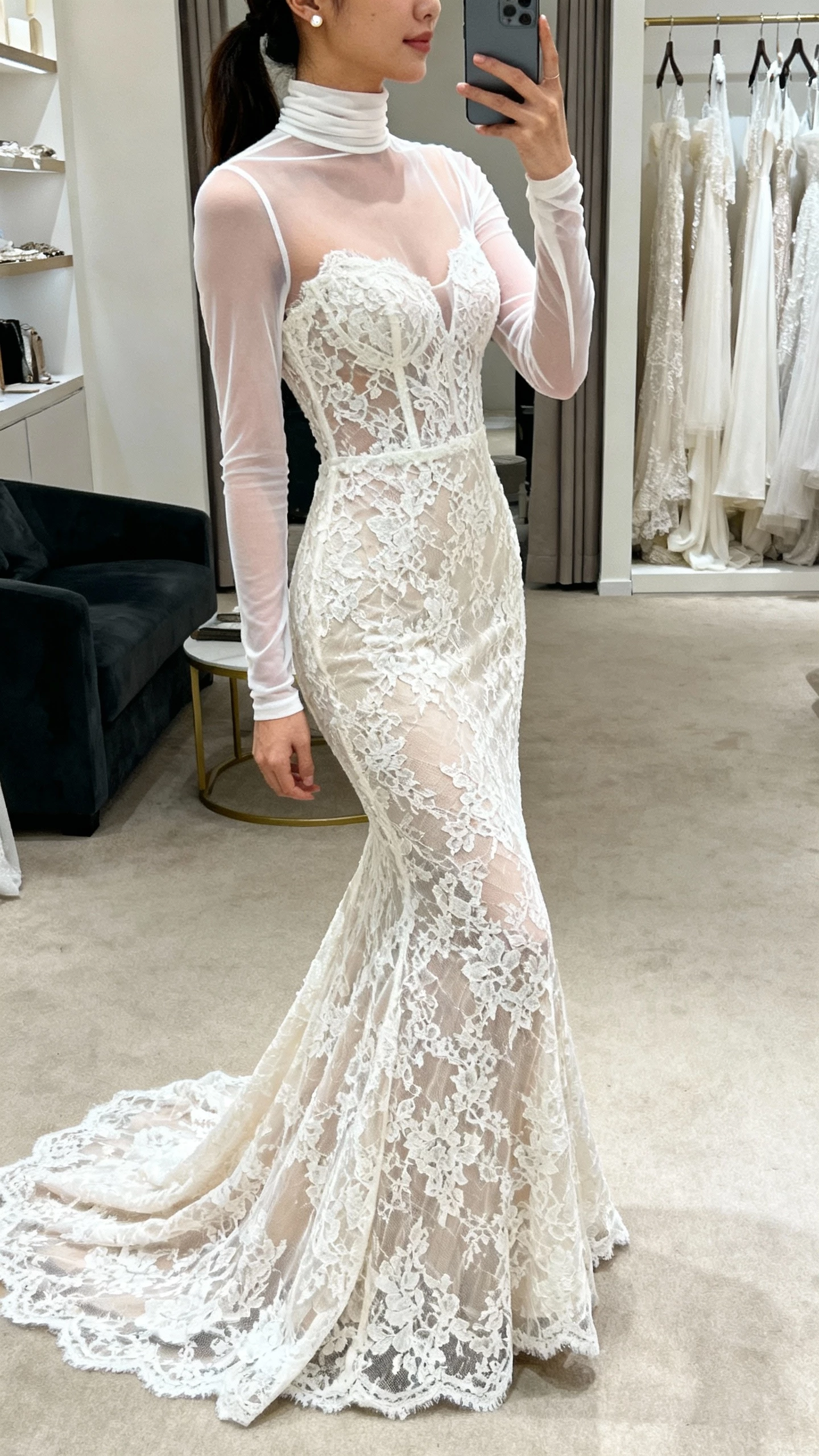 iPhone side-view selfie of a woman wearing a lace overlay mermaid gown with an illusion turtleneck and sheer long yoke, delicate stud earrings, face not visible, boutique fitting room, soft indoor lighting, casual iPhone photo.