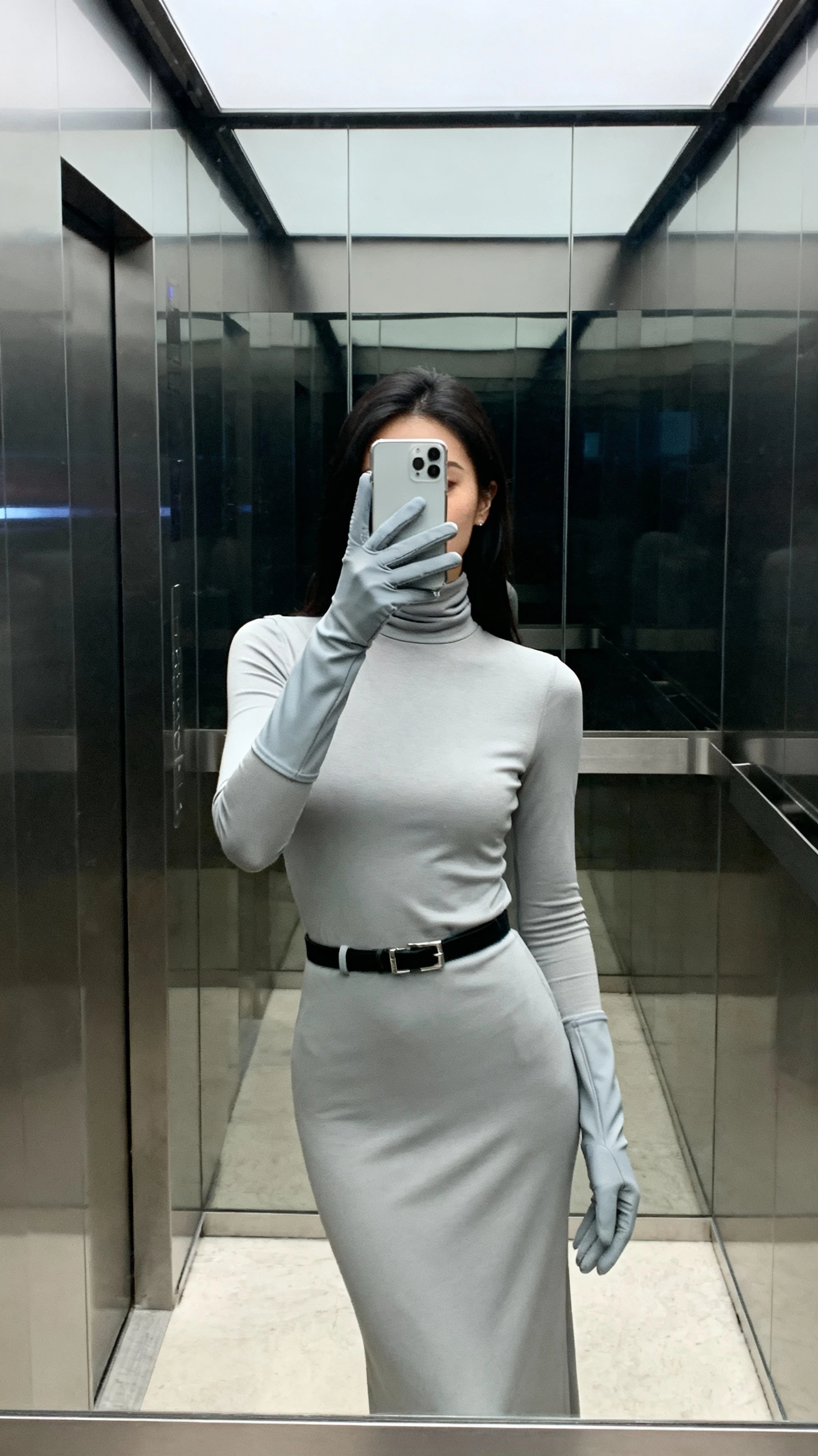 iPhone elevator mirror selfie of a woman wearing matte stretch gloves with a high-neck column dress, sleek belt detail, face not visible, cool indoor lighting, natural iPhone photo quality