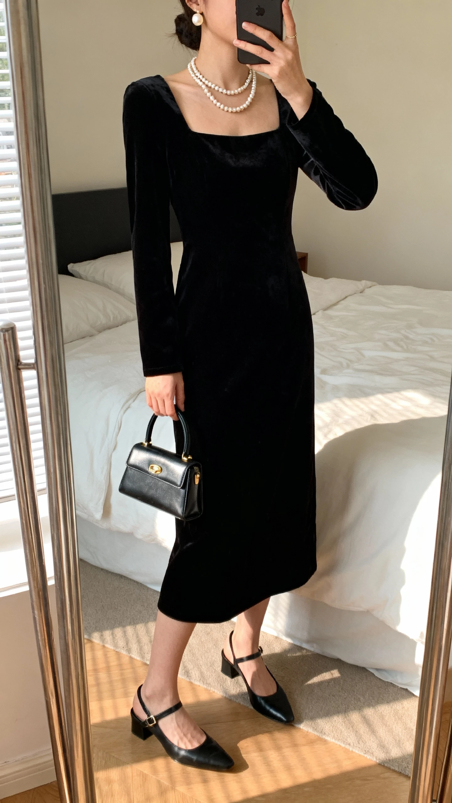 iPhone mirror selfie of a woman in a black velvet square-neck midi with layered pearl necklace and pearl earrings, black slingback heels, mini top-handle bag, face not visible, bedroom mirror, soft afternoon light, natural iPhone aesthetic.