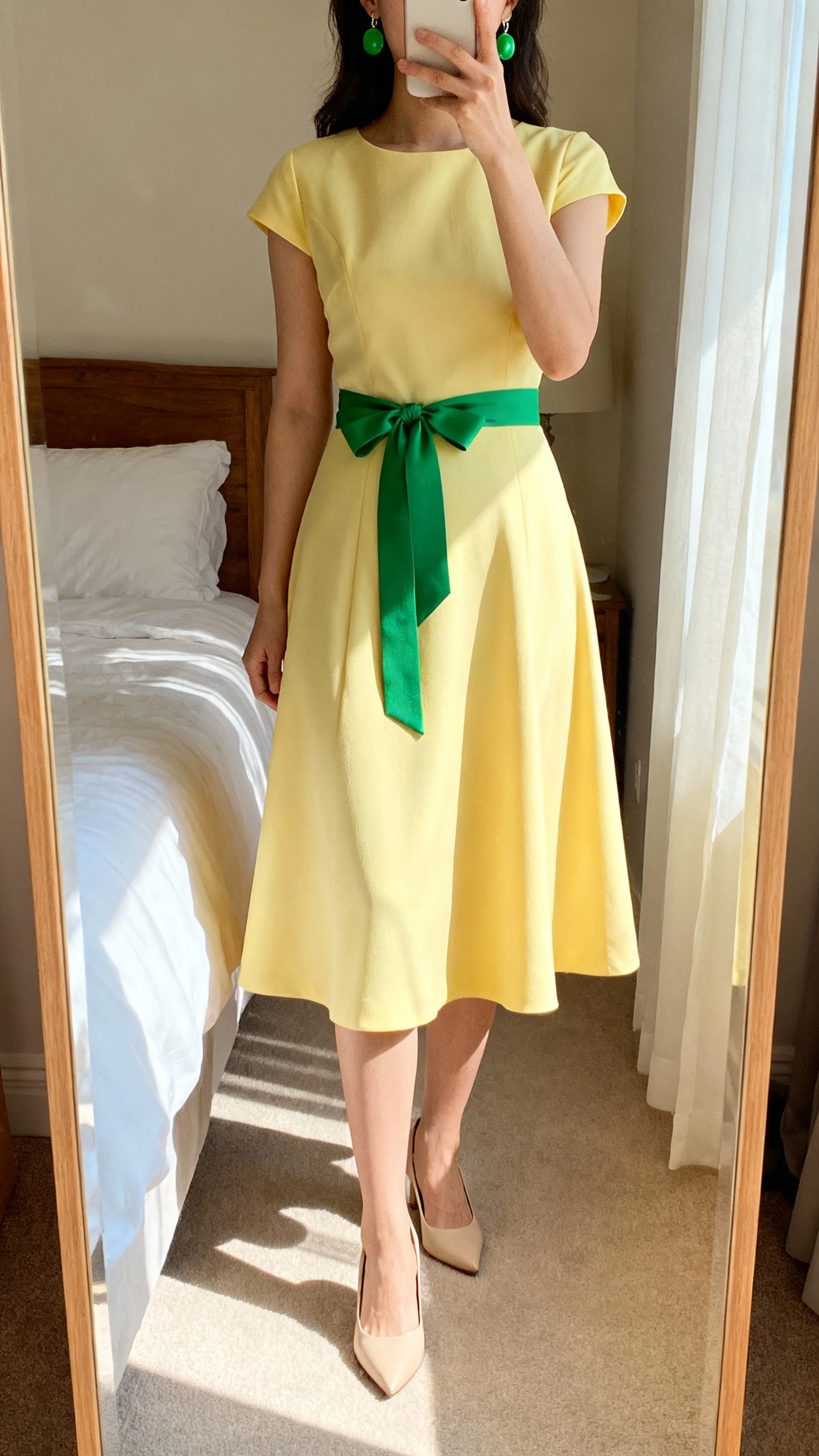 iPhone mirror selfie of a woman in a butter yellow fit-and-flare dress styled with a green ribbon belt and matching green earrings, beige heels, face not visible, bedroom mirror with morning light, natural iPhone photo quality.