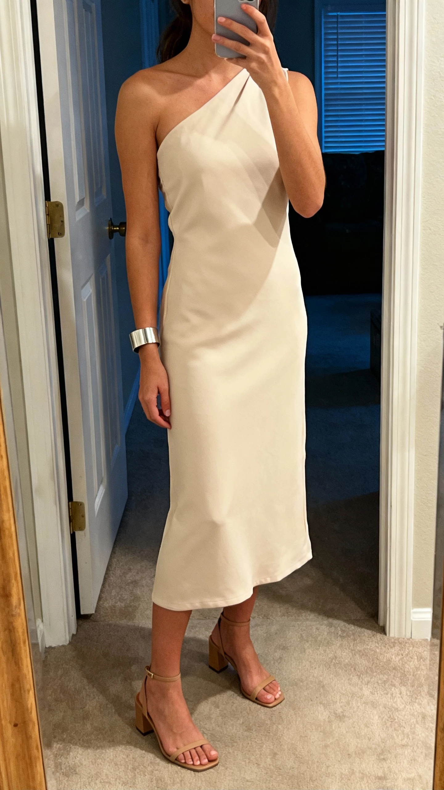 iPhone mirror selfie of a woman in a one-shoulder midi dress with clean lines, minimal heeled sandals, and a sleek cuff bracelet, face not visible, entryway mirror, soft evening light, natural iPhone aesthetic