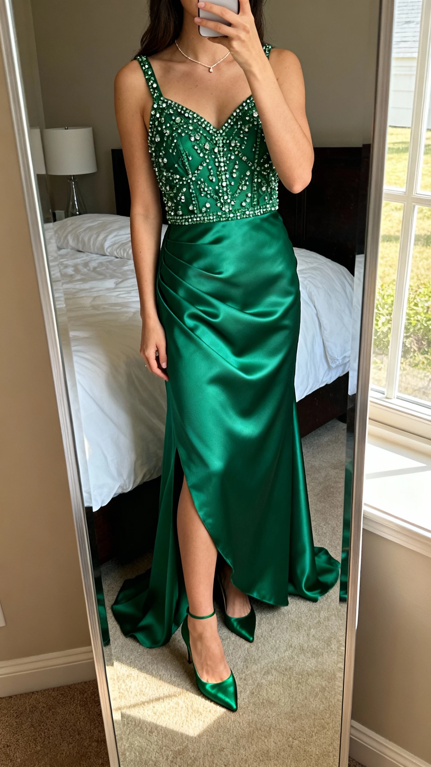 iPhone mirror selfie of a woman in an emerald gown with a beaded bodice and satin skirt combo, dainty necklace, satin heels, face not visible, bedroom full-length mirror, soft afternoon window light, natural iPhone aesthetic.