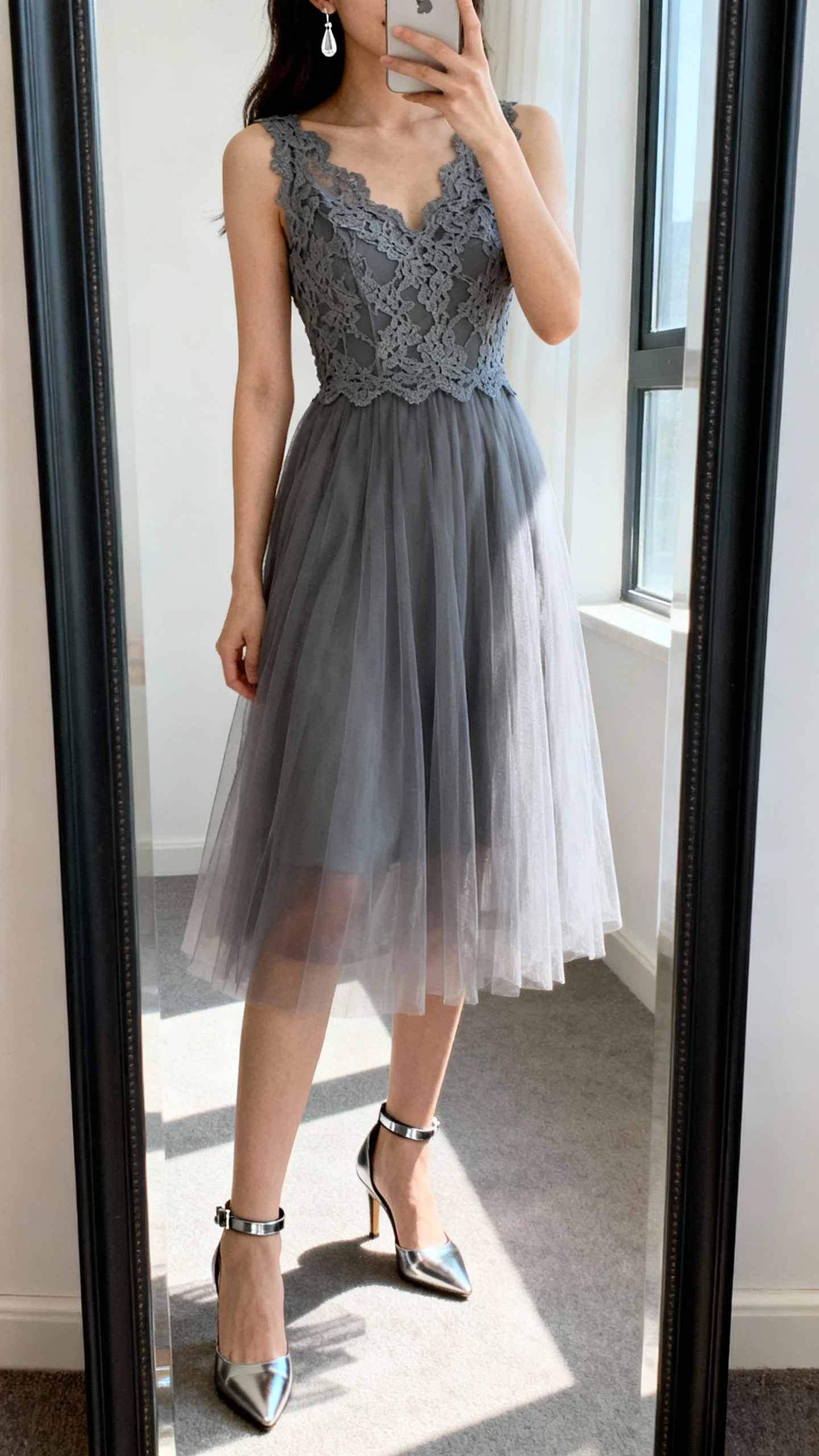 iPhone mirror selfie of a woman wearing a lace bodice with a soft tulle skirt in slate gray, metallic ankle-strap heels, and delicate drop earrings; face not visible, studio-style full-length mirror, bright natural window light, iPhone photo quality.