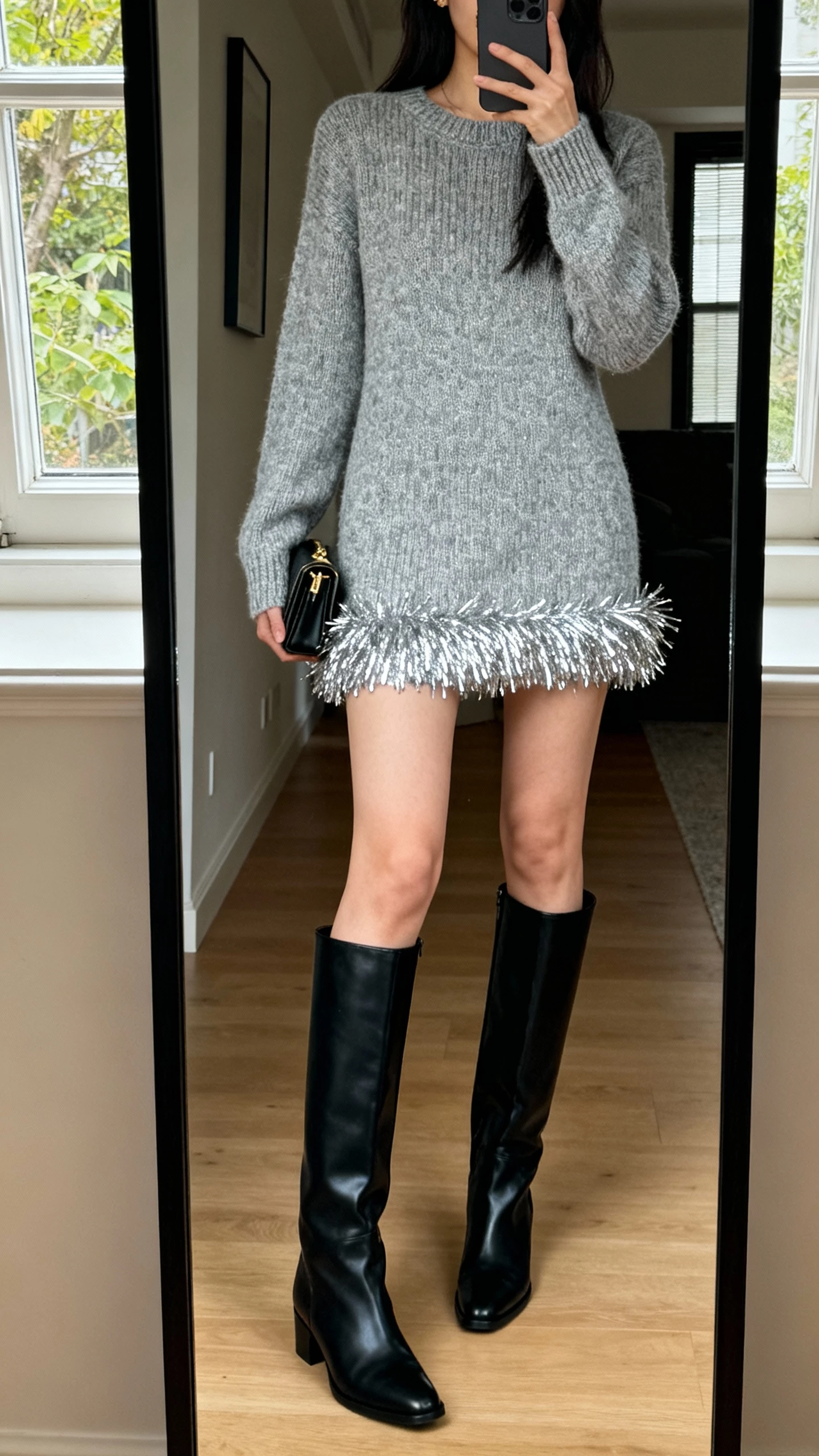 iPhone mirror selfie of a woman wearing a silver-tipped knit dress with tall black boots, small clutch, face not visible, cropped at shoulders, apartment full-length mirror, natural window light, iPhone photo quality