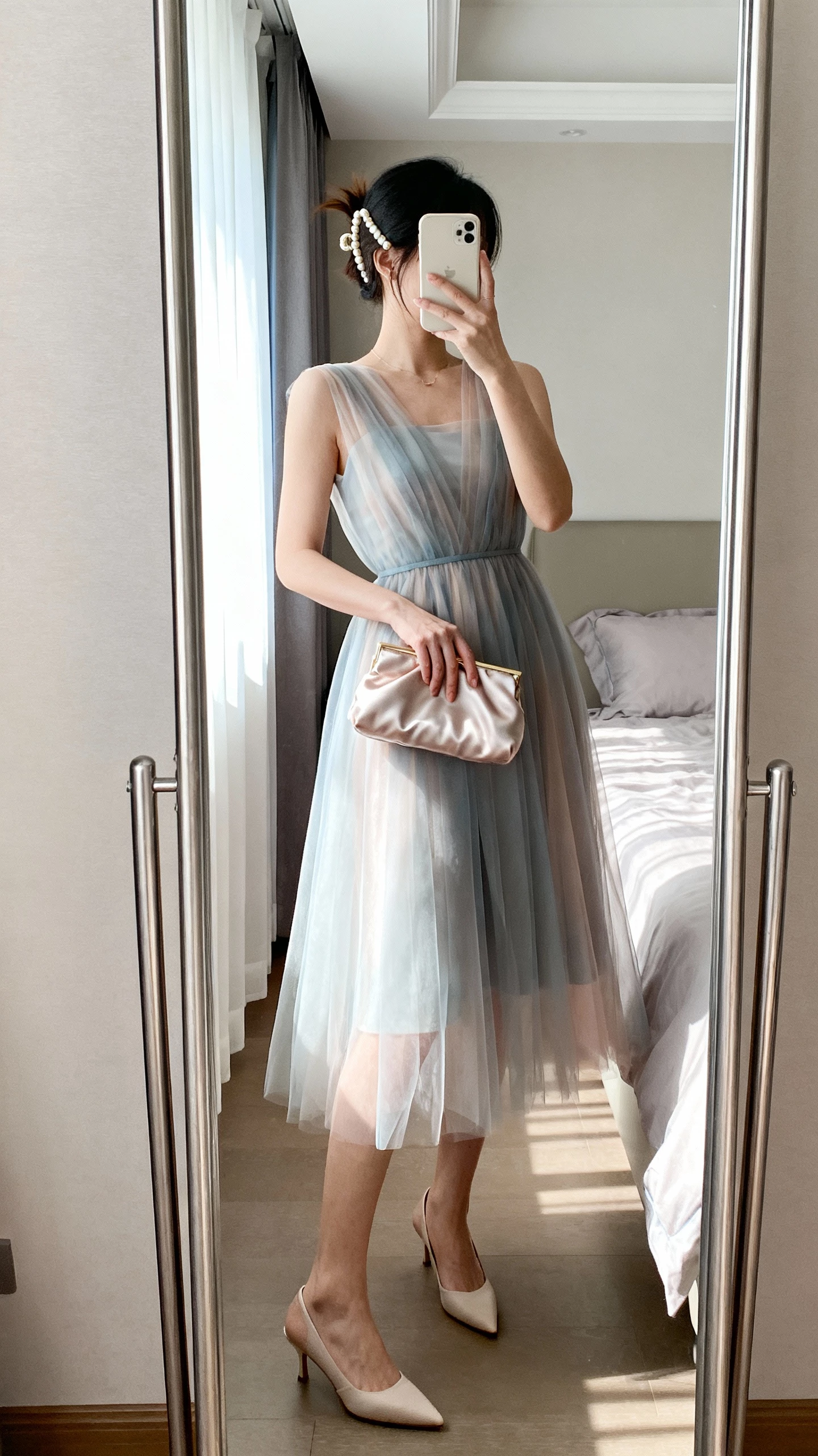 iPhone mirror selfie of a woman wearing an airy organza A-line dress with sheer overlay, kitten heels, pearl hair clip, and a satin clutch, face not visible, bedroom full-length mirror, soft daylight from window, casual iPhone aesthetic