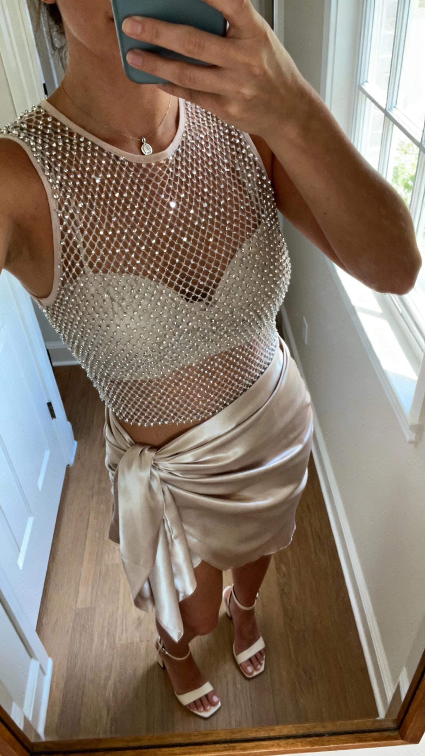 iPhone neck-down selfie showing a rhinestone mesh top layered under a satin wrap dress, subtle pendant, heeled sandals, face not visible, hallway mirror at home, afternoon window light, natural iPhone photo.