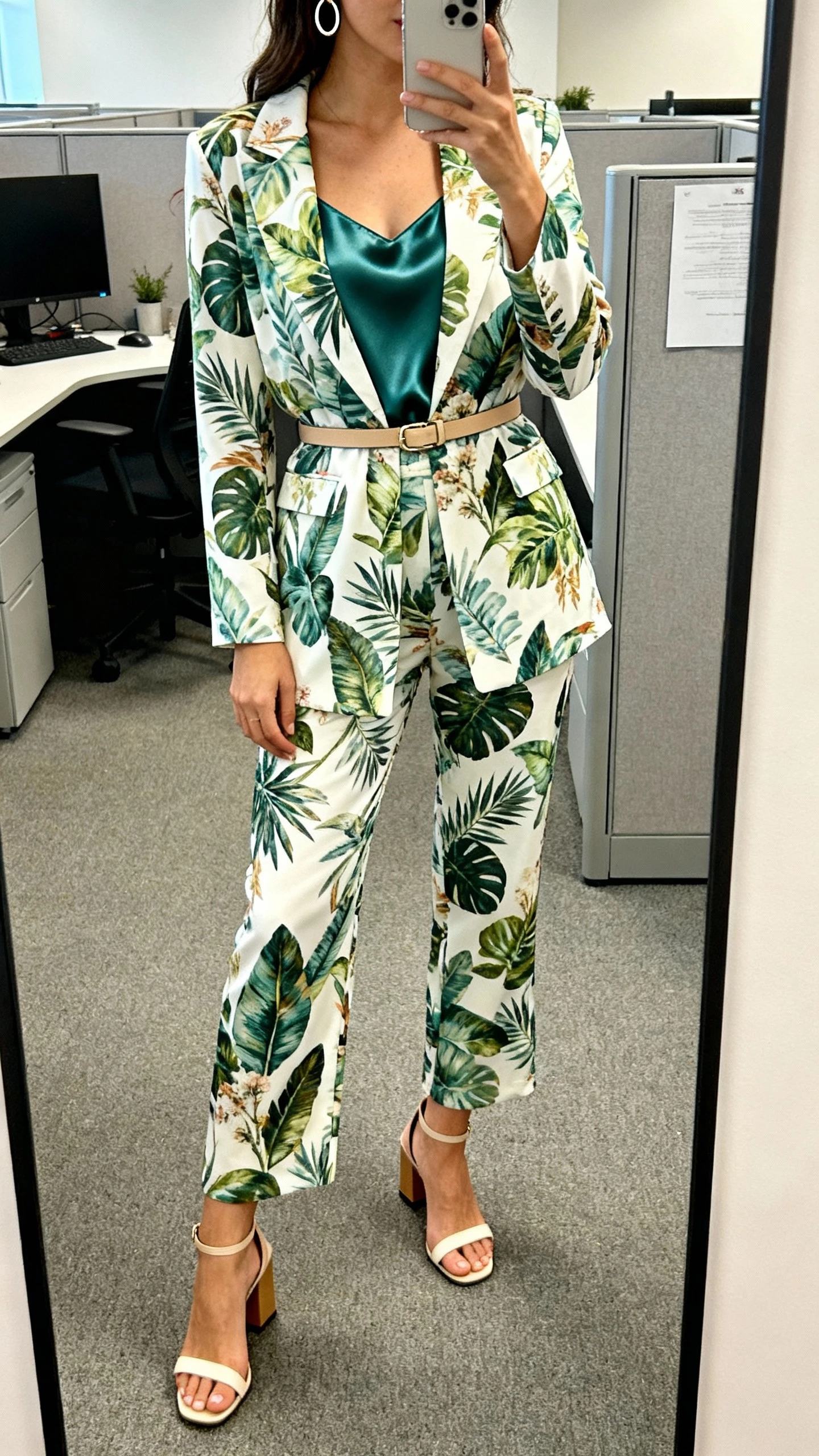 iPhone office mirror selfie of a woman wearing a botanical print suit set with a satin cami, slim belt, block-heel sandals, simple hoops, face not visible, cropped at shoulders, soft indoor lighting, natural iPhone photo quality