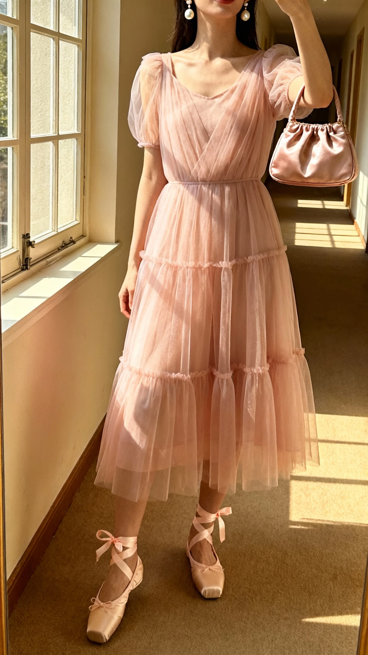 iPhone selfie cropped at shoulders showing a woman in a blush tulle midi dress with soft layers, ballet flats with ribbon ties, pearl drop earrings, and a satin mini bag, face not visible, taken in a sunlit hallway near a window, natural iPhone aesthetic.