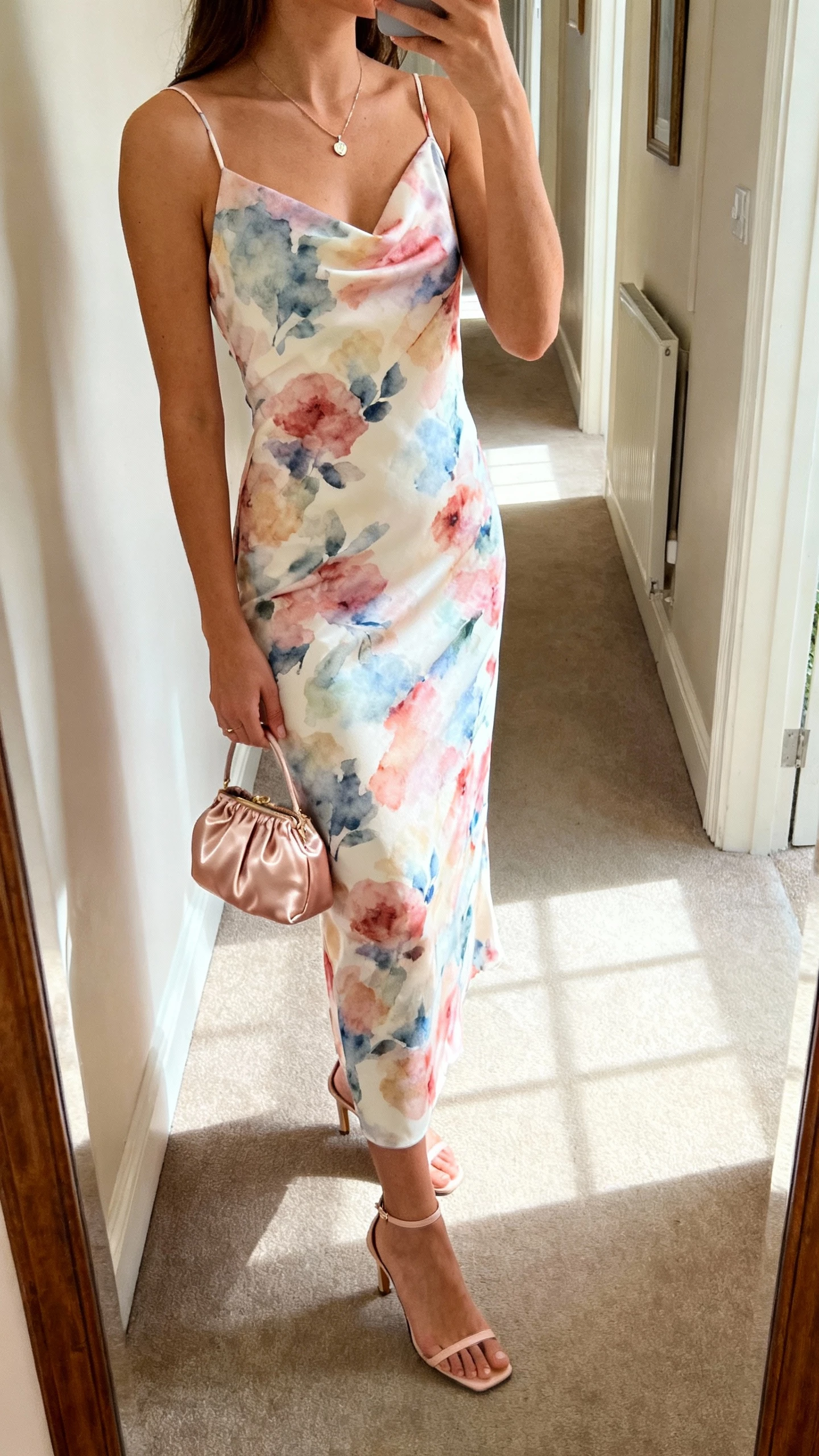 iPhone side-angle selfie showing a woman in a watercolor floral slip dress with bias cut, slim ankle-strap heels, dainty pendant necklace, and a satin mini bag, face not visible, hallway mirror before a wedding, afternoon natural light, casual iPhone aesthetic.