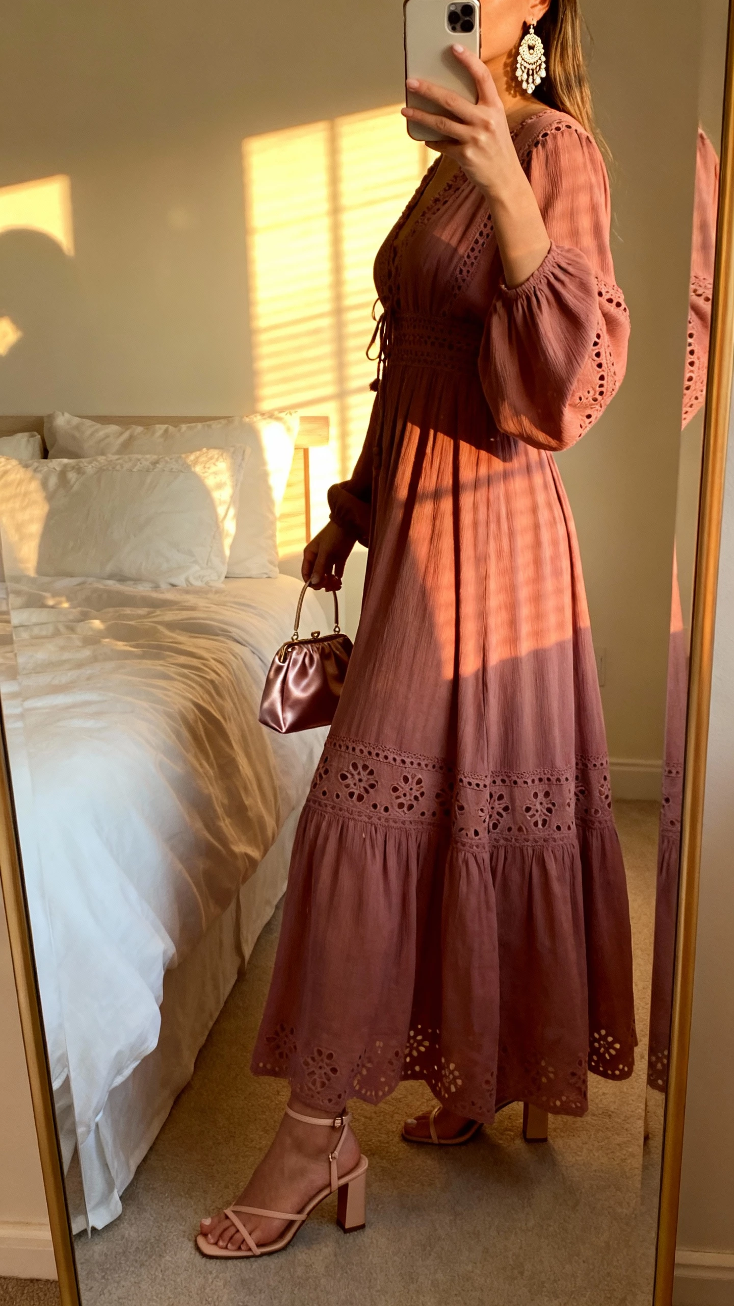 iPhone side-view mirror selfie of a woman wearing a dusty rose boho gown with cutwork details, delicate heeled sandals, chandelier earrings, satin mini bag, face not visible, bedroom mirror with late-afternoon window light, natural iPhone photo quality.