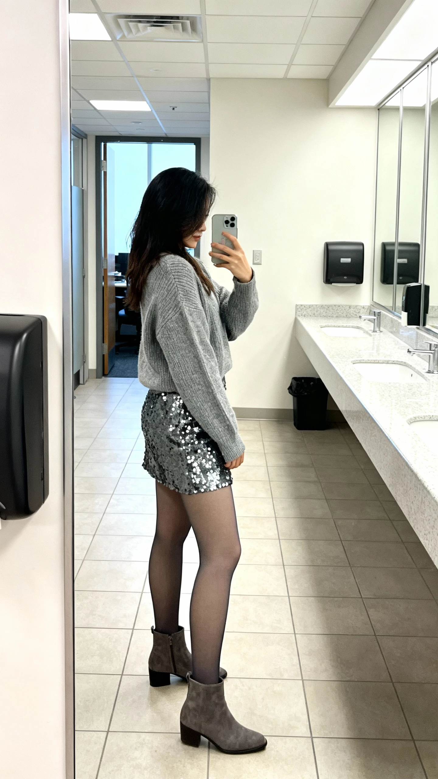 iPhone side-view selfie of a woman wearing a gunmetal sequin skirt with a cashmere-feel sweater, opaque tights, ankle boots, face not visible, office restroom mirror, bright indoor lighting, casual iPhone quality.