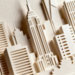 Closeup layered paper-cut city skyline on heavy cardstock, soft shadows