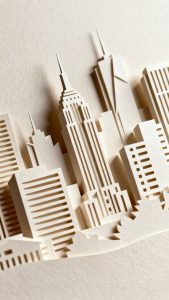 Closeup layered paper-cut city skyline on heavy cardstock, soft shadows