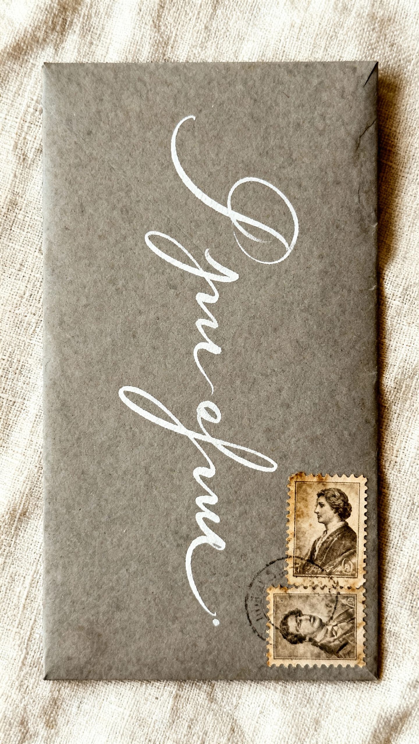 Slate envelope with white ink calligraphy, vintage tonal stamps, soft linen texture