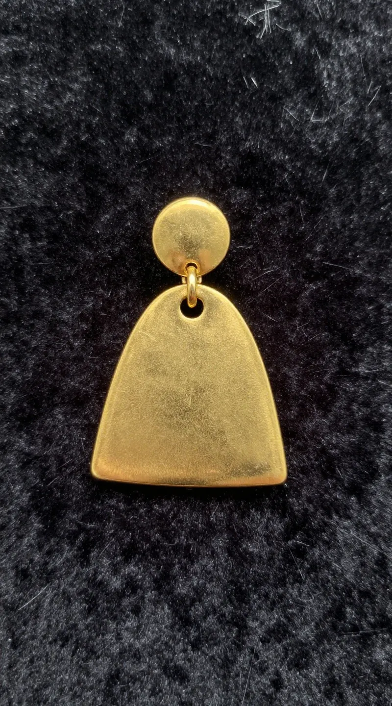 **Single gold statement earring on velvet backdrop**