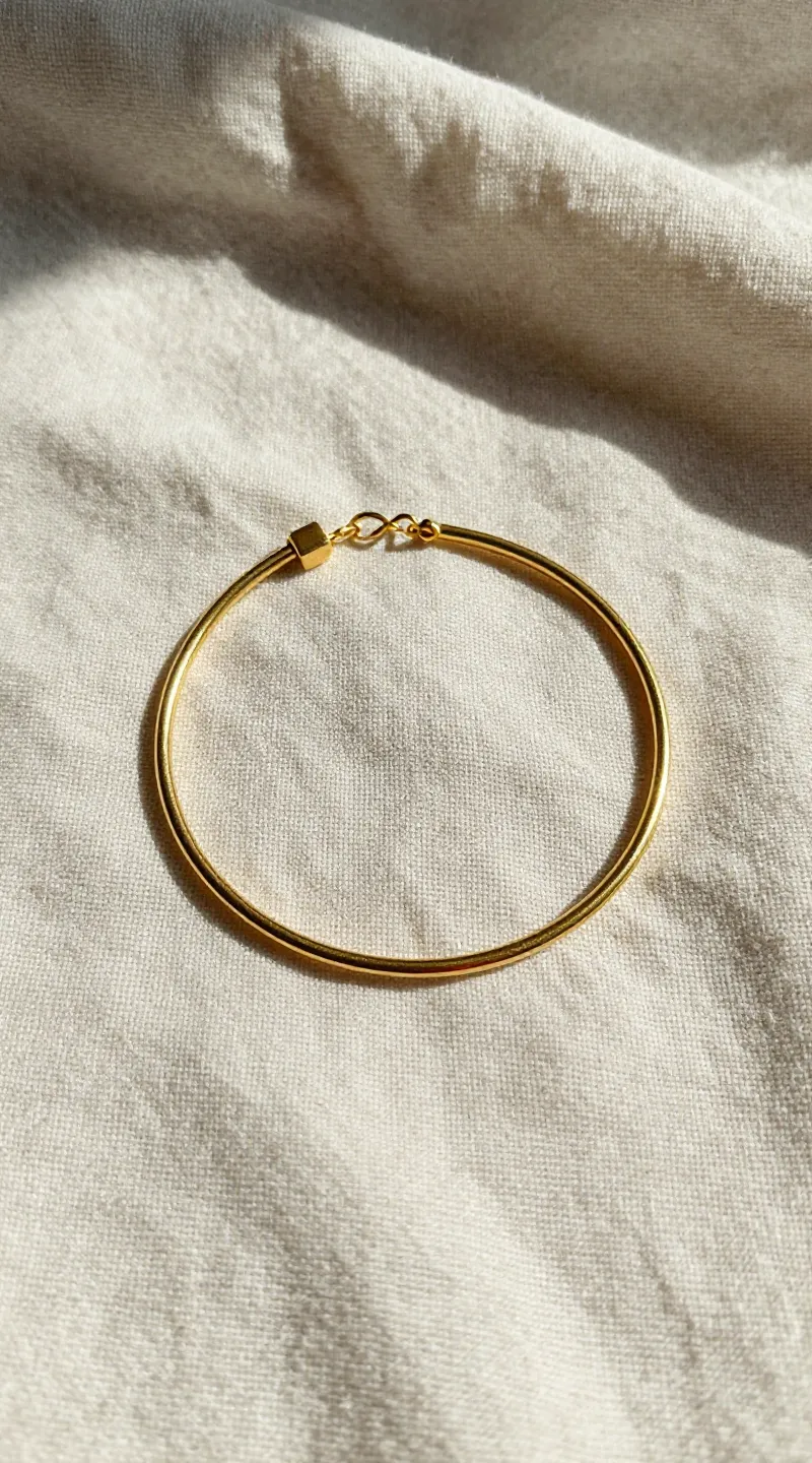 **Single delicate gold bracelet on sunlit linen fabric**
