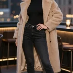 **Image Prompt:** "A stylish woman posing confidently in a luxurious urban setting at dusk, wearing an effortlessly sexy Valentine's Day outfit. She has on a soft, neutral beige teddy bear coat draped off one shoulder, revealing a sleek black bodysuit underneath. The bodysuit pairs perfectly with high-waisted, fitted jeans, and she completes the look with chic black ankle boots. Her accessories are minimal—just a pair of gold hoop earrings and a delicate watch—while her bold red lip adds a touch of drama. The scene is softly lit with warm ambient lighting, perhaps near a rooftop bar or city street, creating an intimate yet stylish atmosphere. Her pose is relaxed yet alluring, with one hand resting on her hip and a slight smile, embodying cozy seduction."