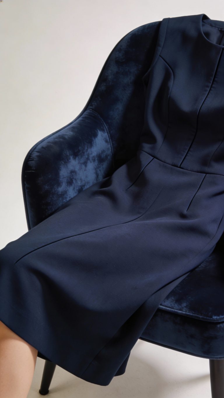 **Tailored navy midi dress draped over velvet chair**