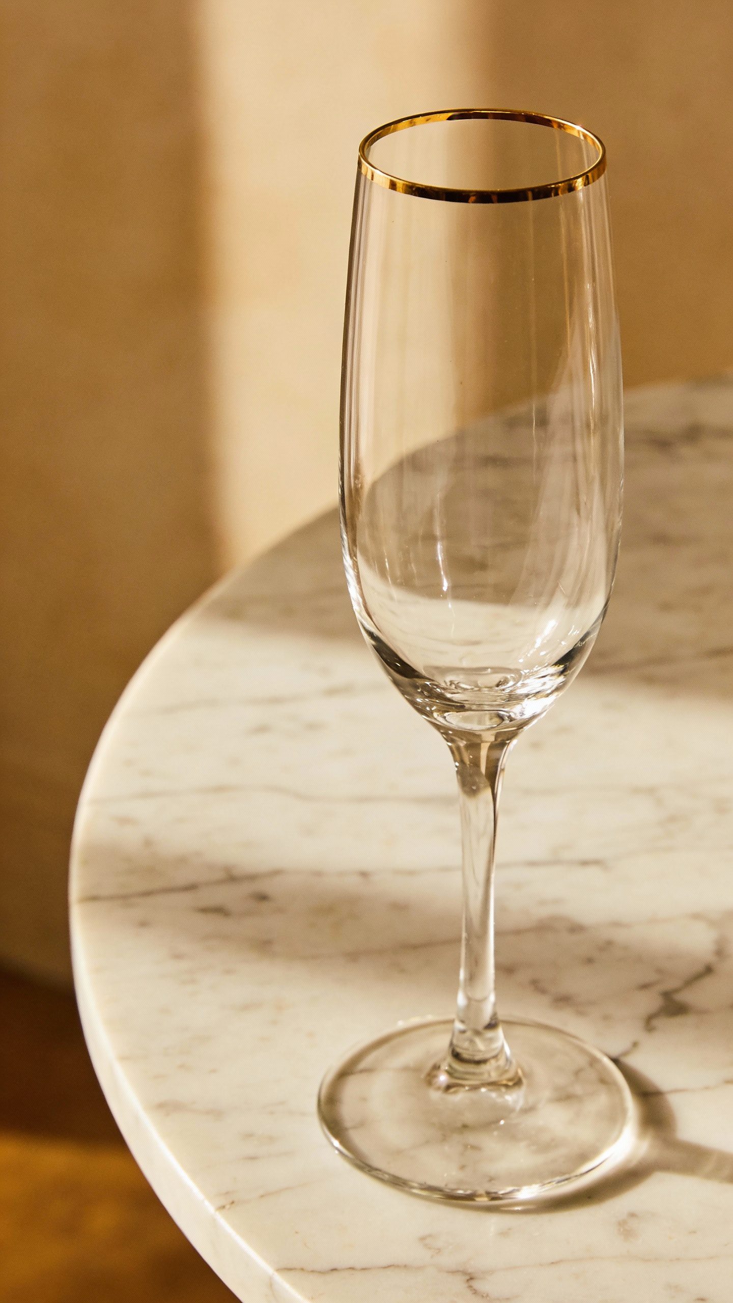 **Single champagne flute with gold rim on marble table**