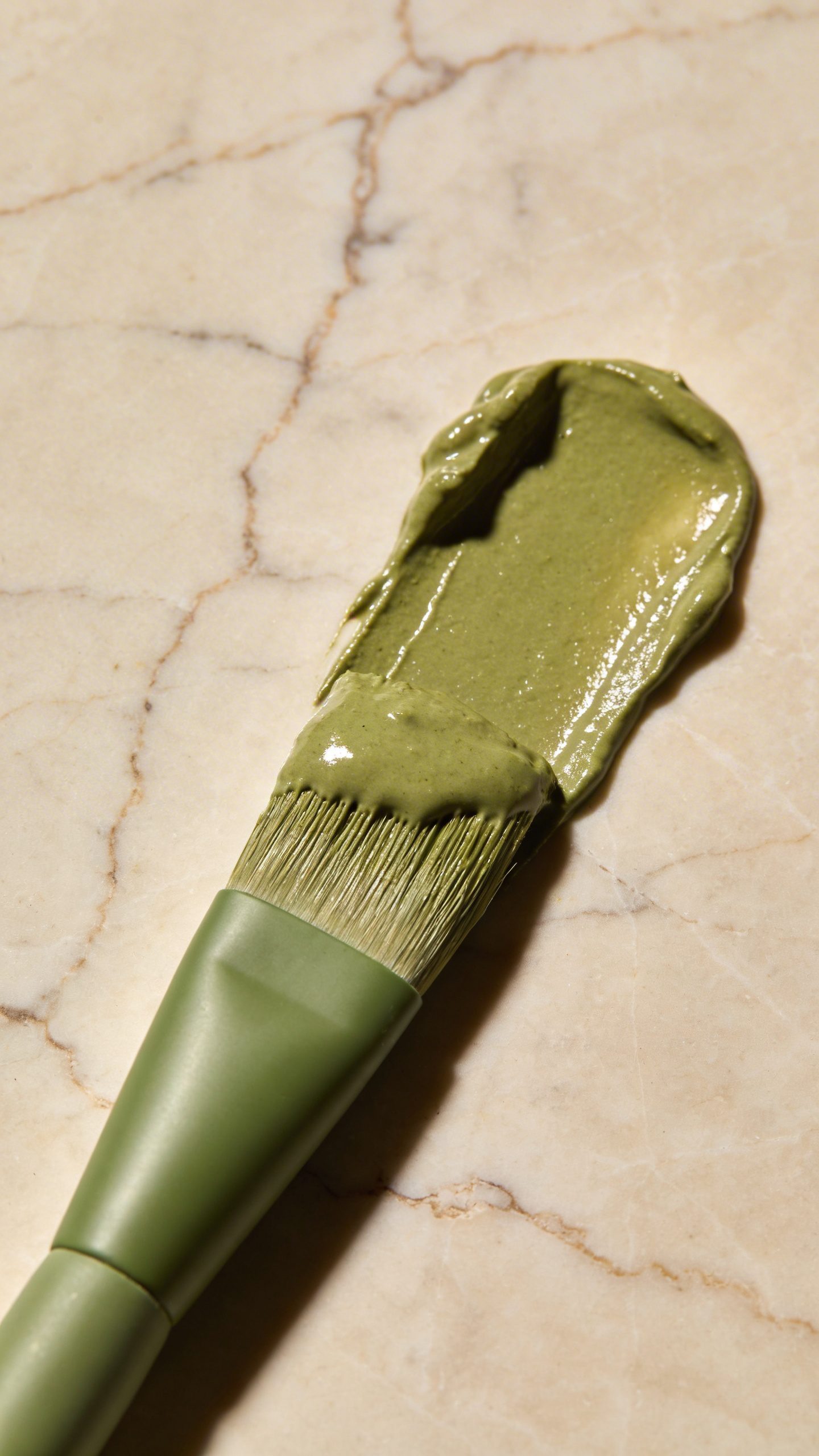 single clay mask brush with green tea paste, marble background