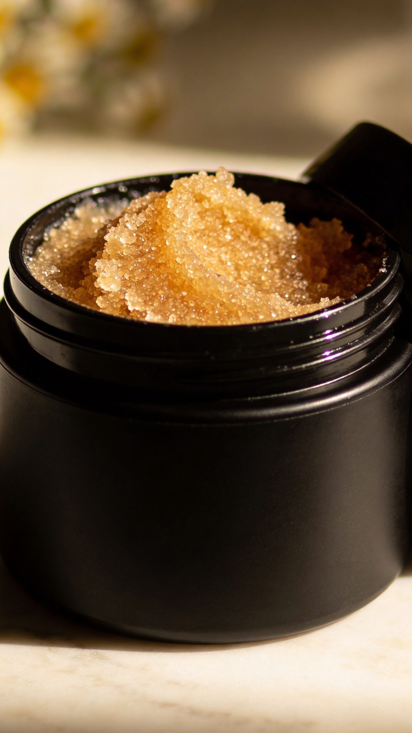 closeup of open sugar body scrub in matte black jar